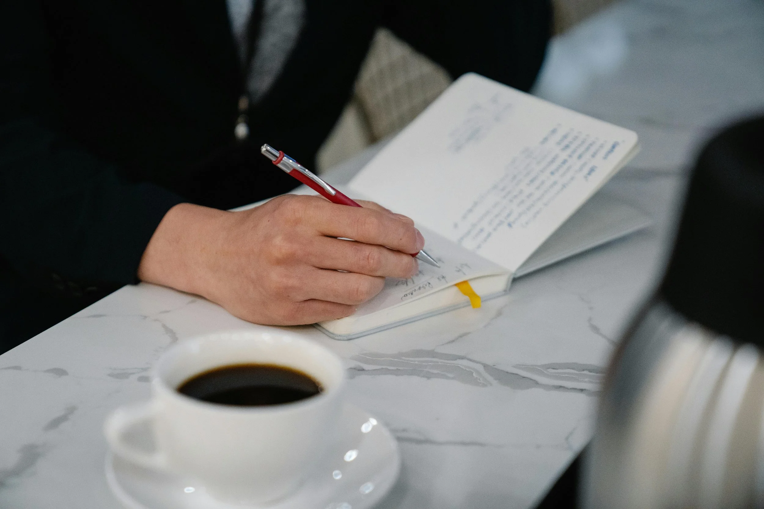 Person writing goals and notes in a notebook at a desk.