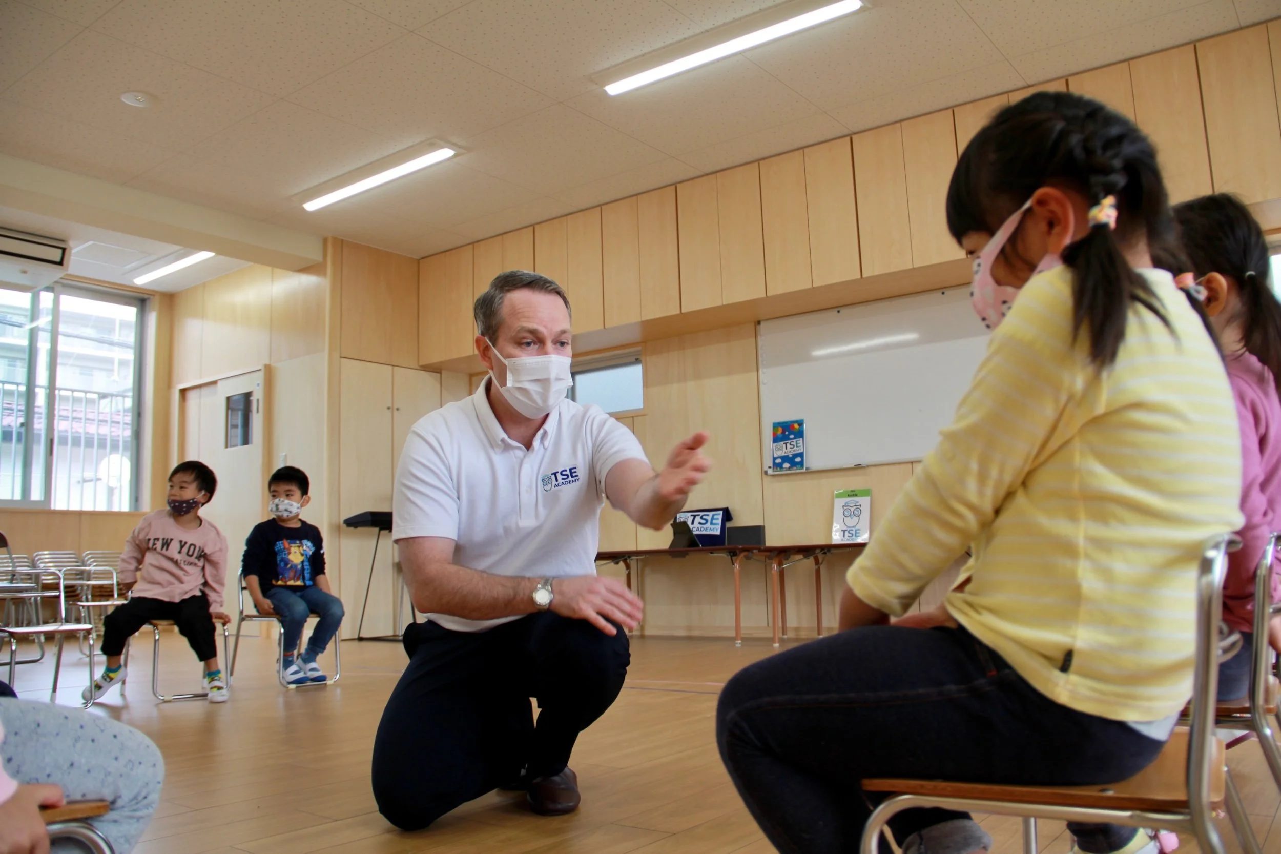 教師と学生たちが教室でマスクを着用して座っている。