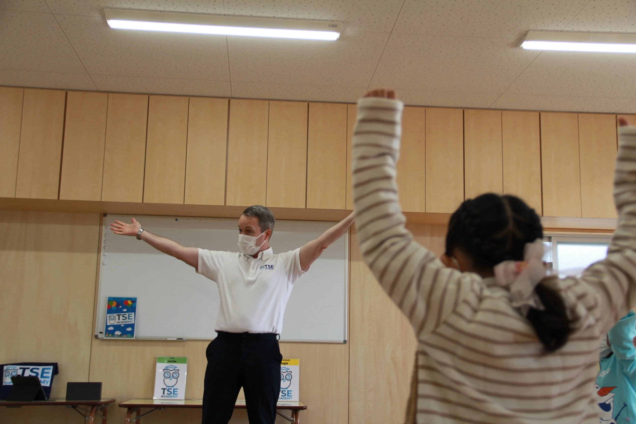 教室で指導中のマスクをした先生と腕を上げている生徒。