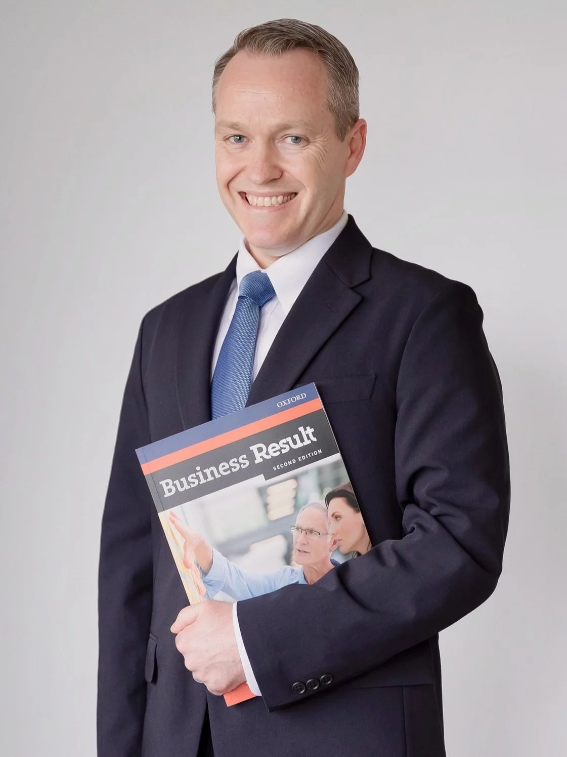 スーツを着た男性が、「Business Result」と書かれた本を持って微笑んでいる。