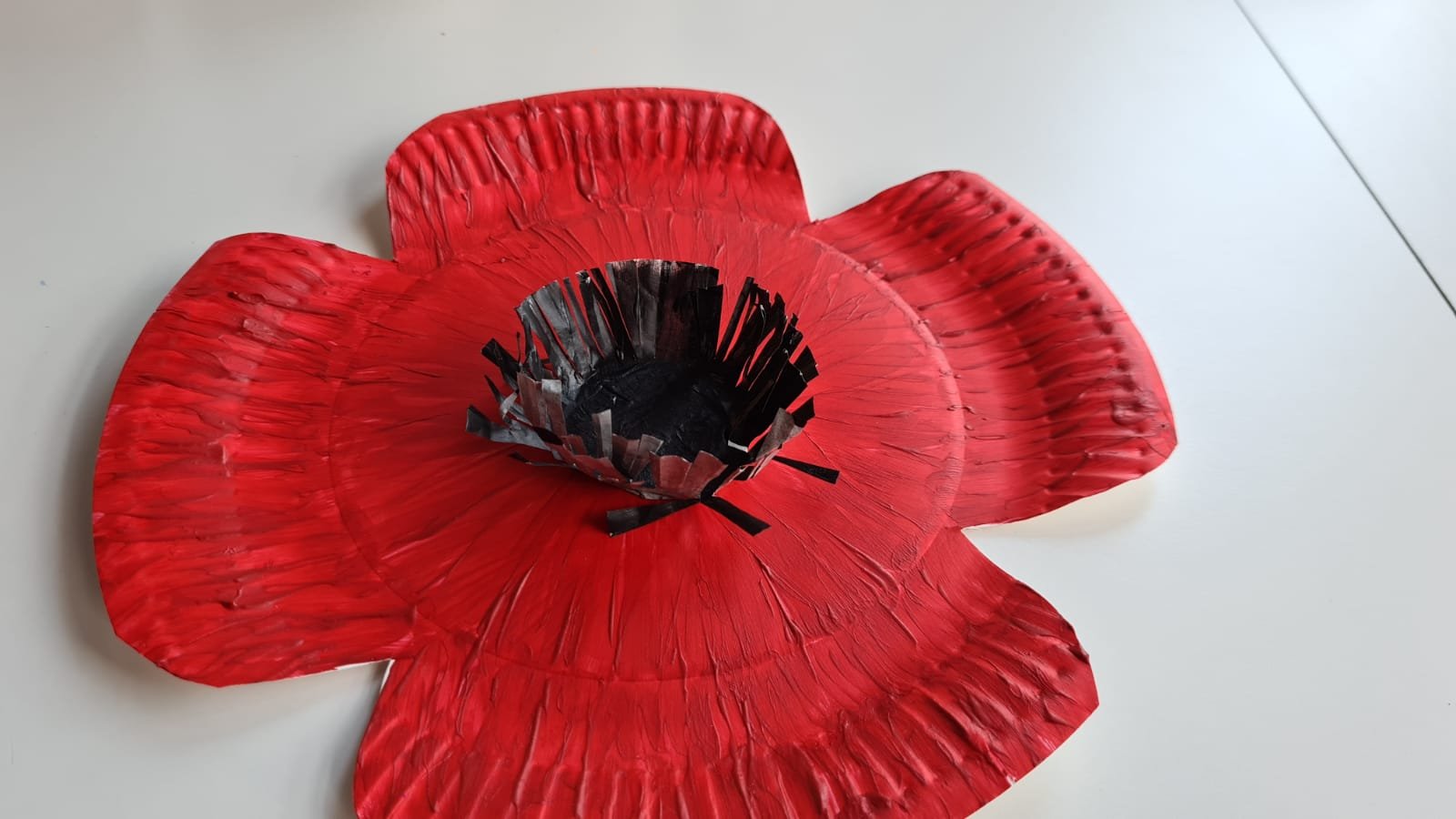 Paper plate cut into poppy shape and painted red with cupcake black stamen glued to middle