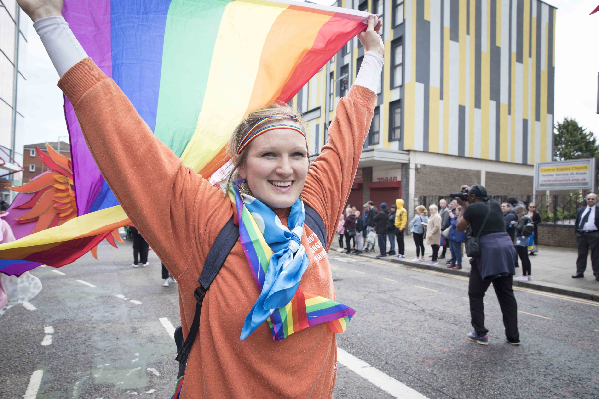 Member of the Pride In Luton carnival group holding pride flag and smiling in Luton Carnival parade 2022