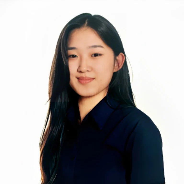 A young woman with long black hair wearing a dark blue shirt, smiling softly against a plain white background.