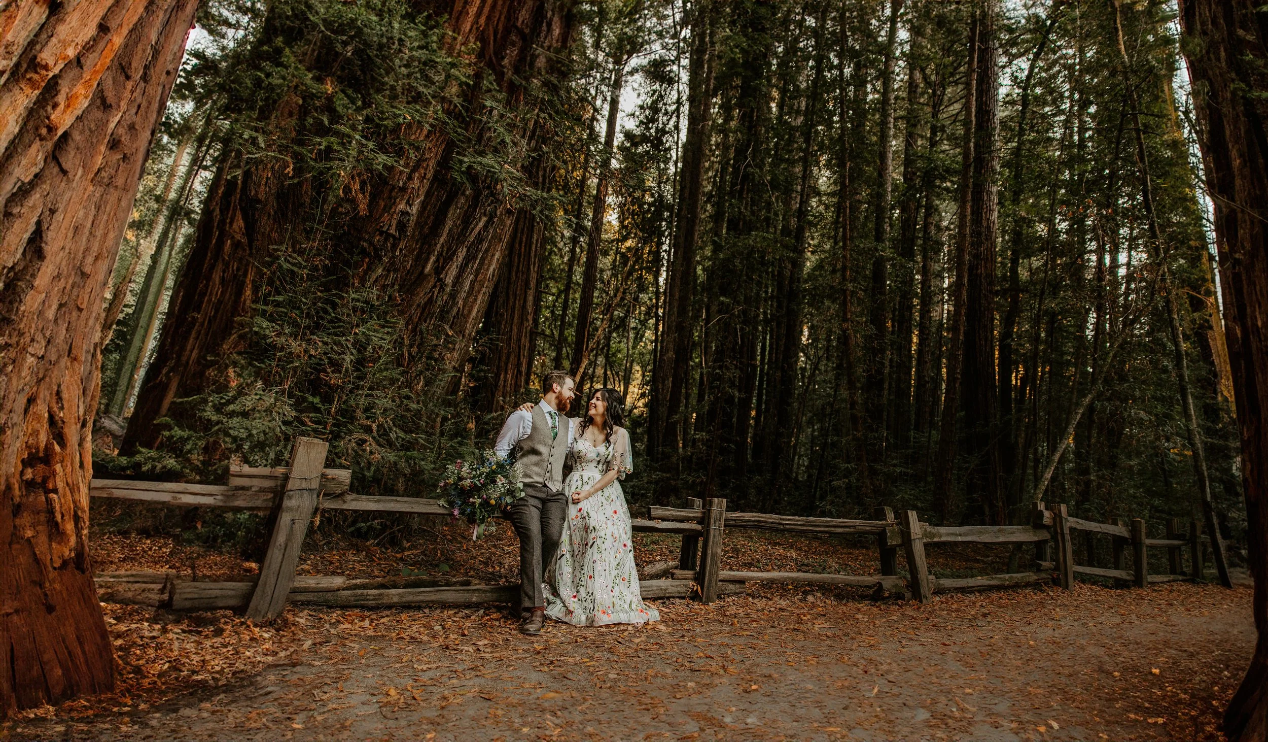 Couple sharing a romantic moment on the Redwood Grove trail at Henry Cowell Redwoods State Park in fall, bride in floral dress with wildflower bouquet