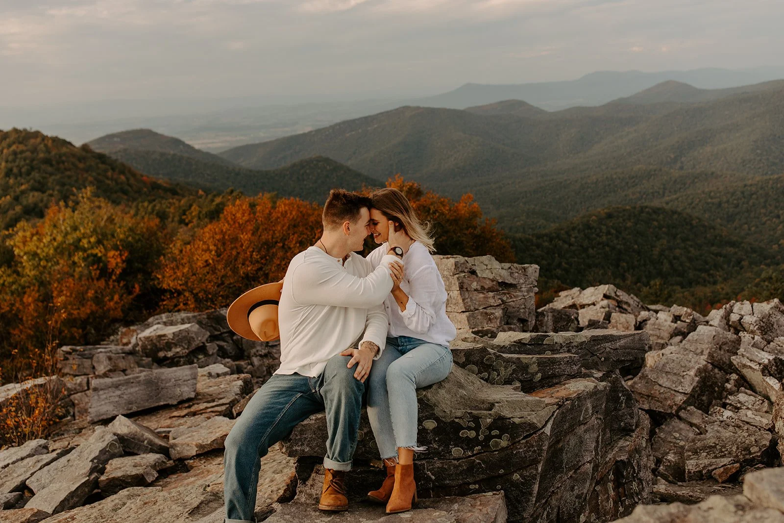 Couple sitting on rocky overlook with fall foliage and mountain views in Shenandoah National Park