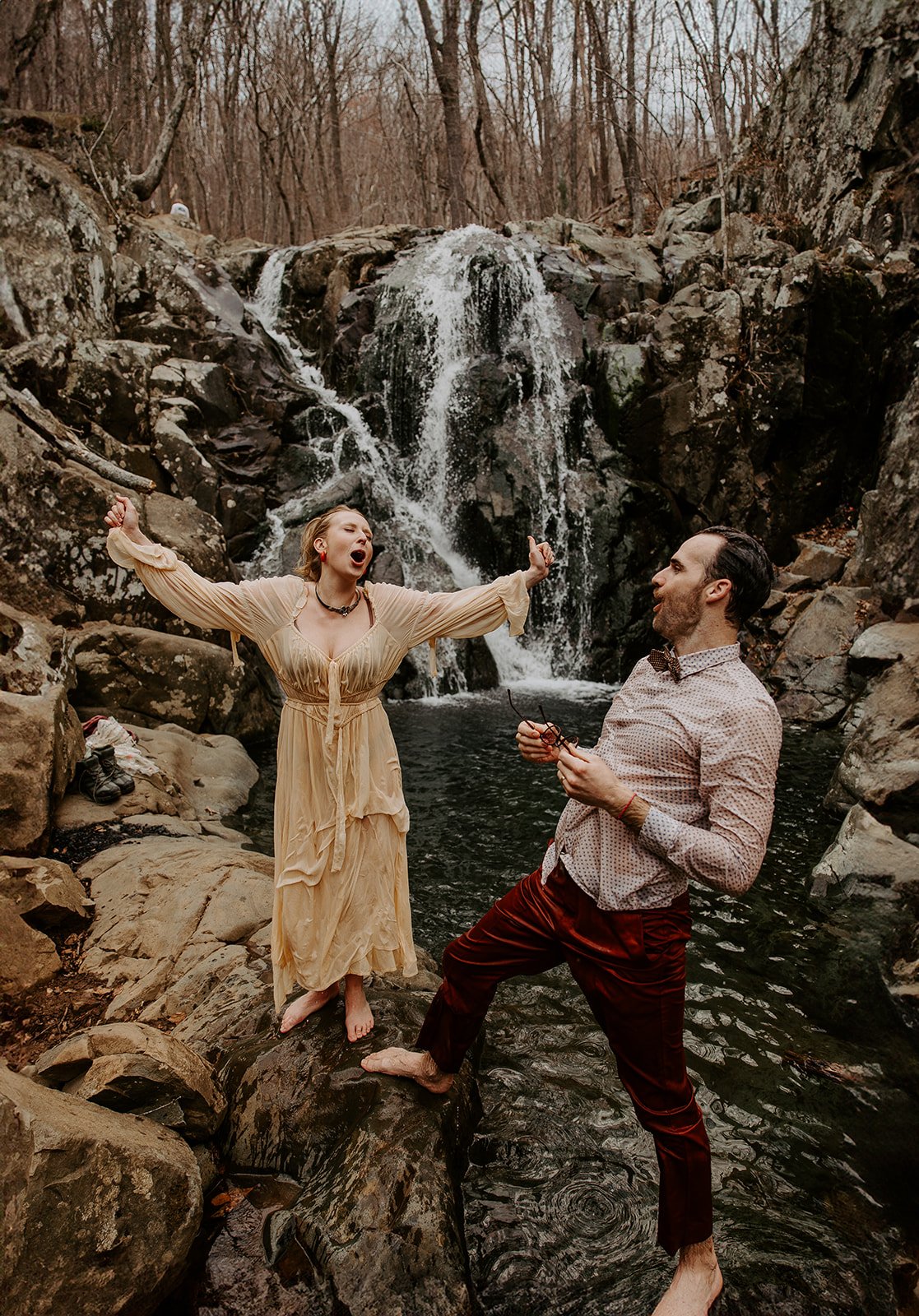 Playful couple celebrating beside Rose River Falls waterfall after an adventure elopement