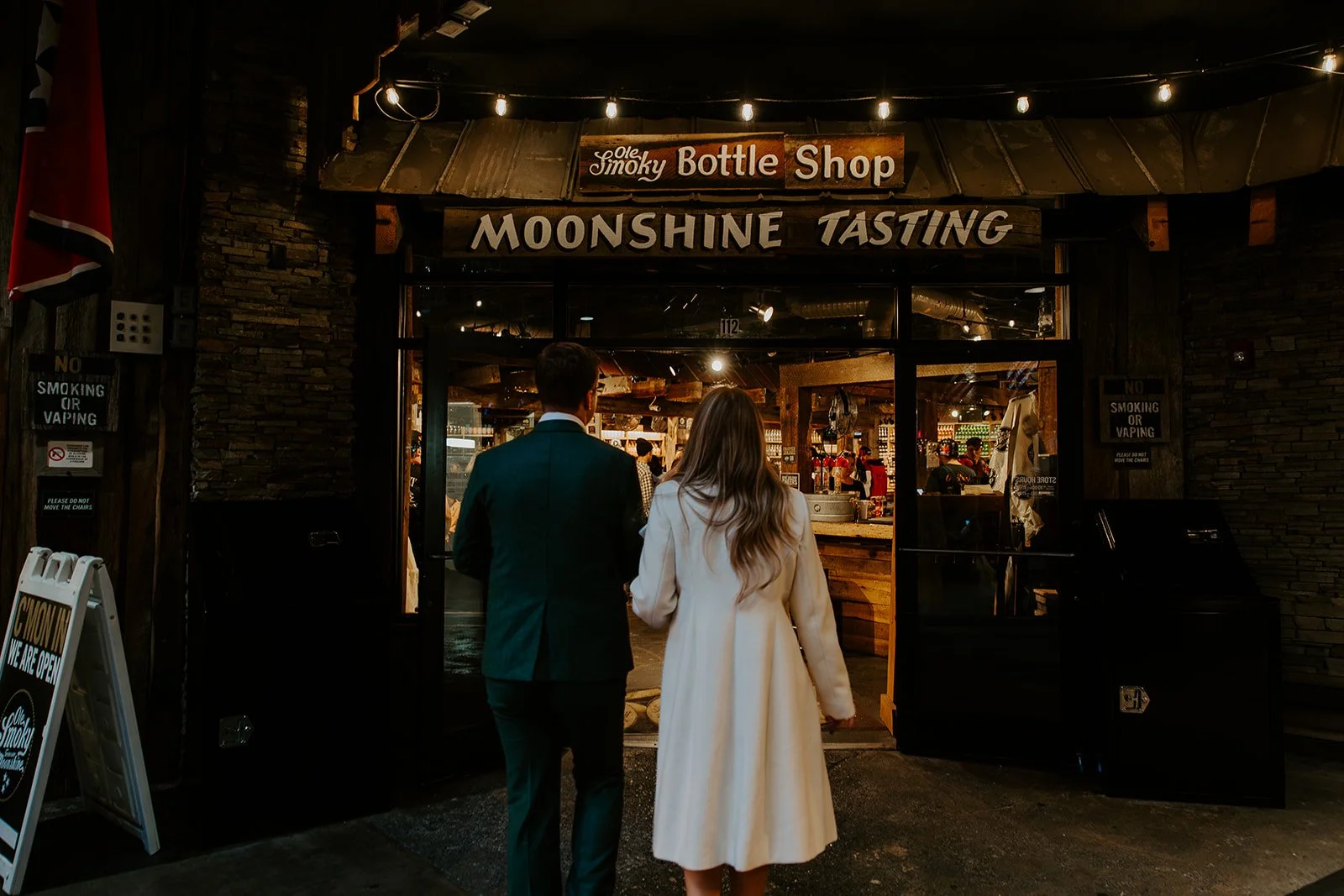 Newlywed couple in wedding attire entering Ole Smoky Bottle Shop for moonshine tasting in downtown Gatlinburg Tennessee after their elopement