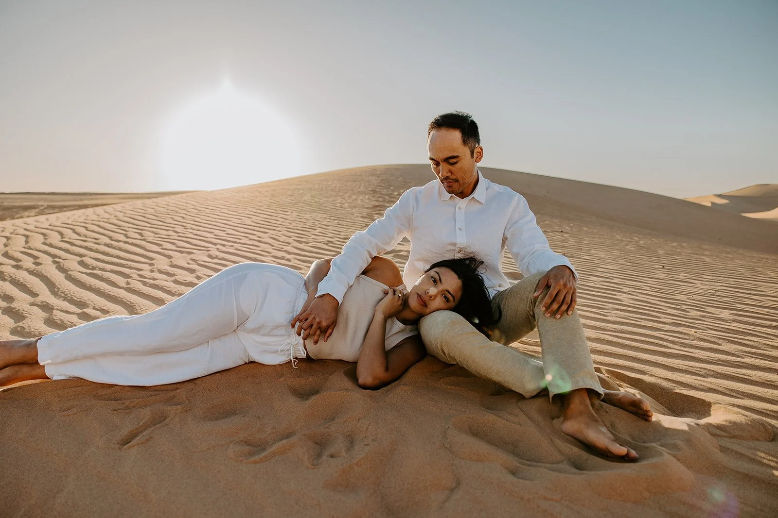 Couple relaxing together on the sand at Hugh T. Osborne Lookout in the Imperial Sand Dunes at Glamis during a golden hour engagement session