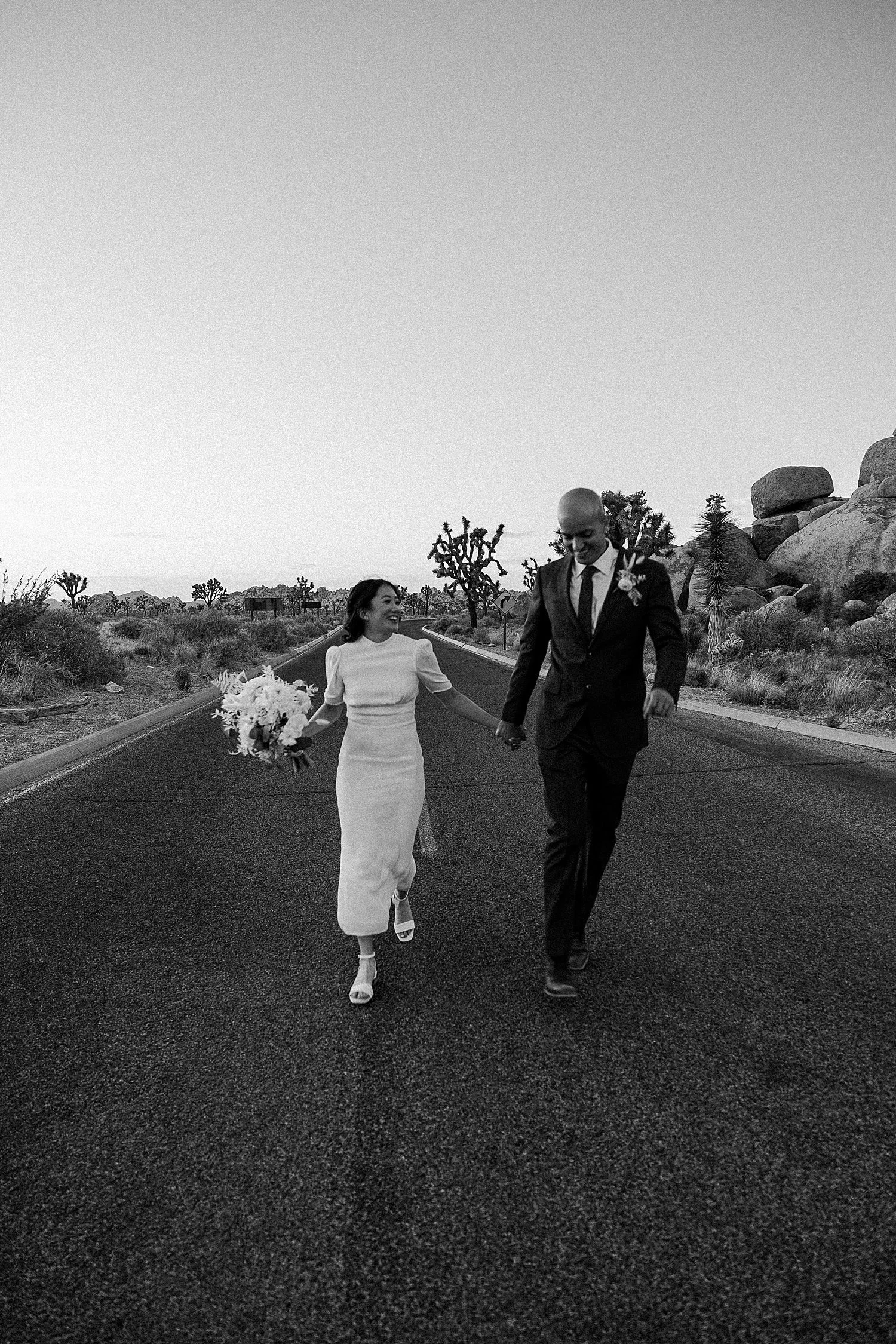 Black and white out of focus photo of the bride and groom holding hands and running down the road in Joshua Tree National Park