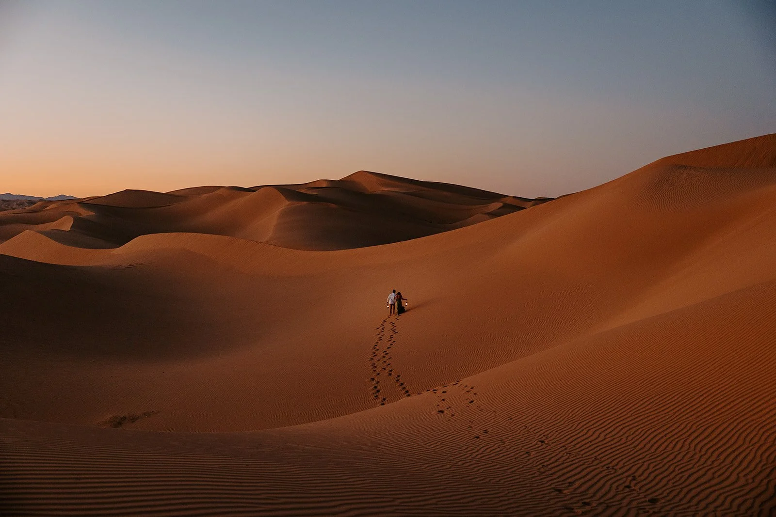couple walking across sweeping sand dunes during an adventurous sand dunes elopement