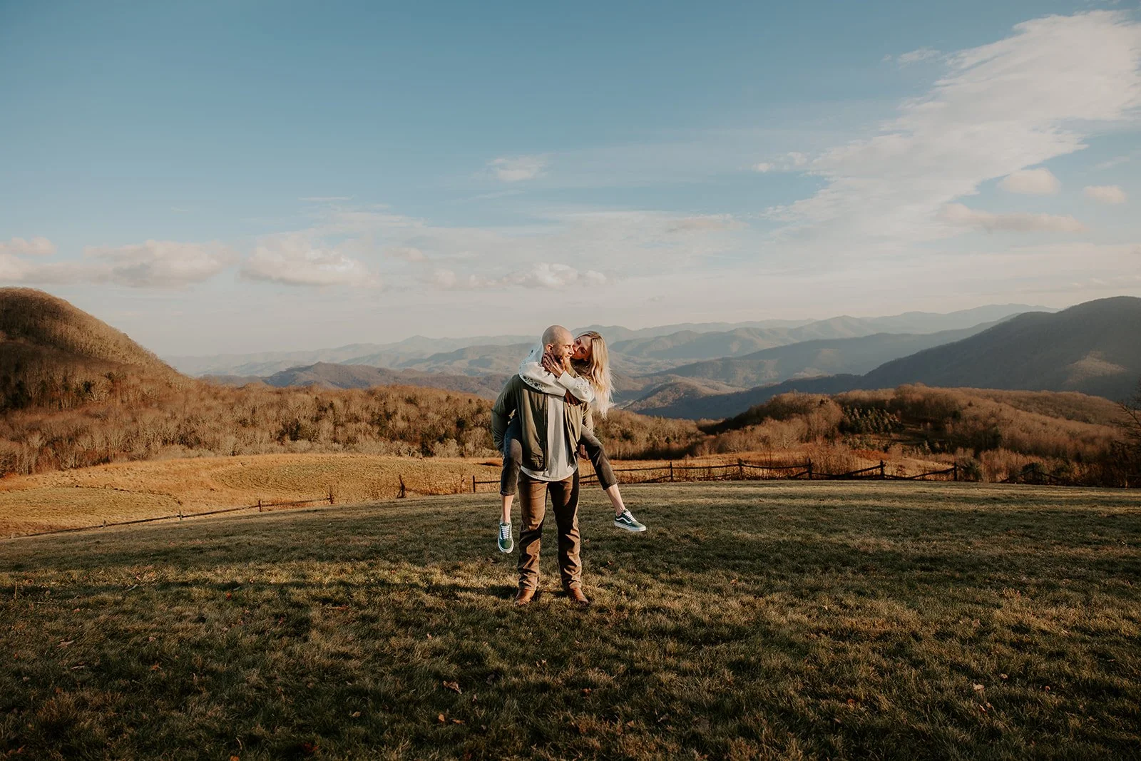 Partner giving the other a piggyback ride at golden hour in an open Smoky Mountain meadow with warm light on the ridgelines behind them