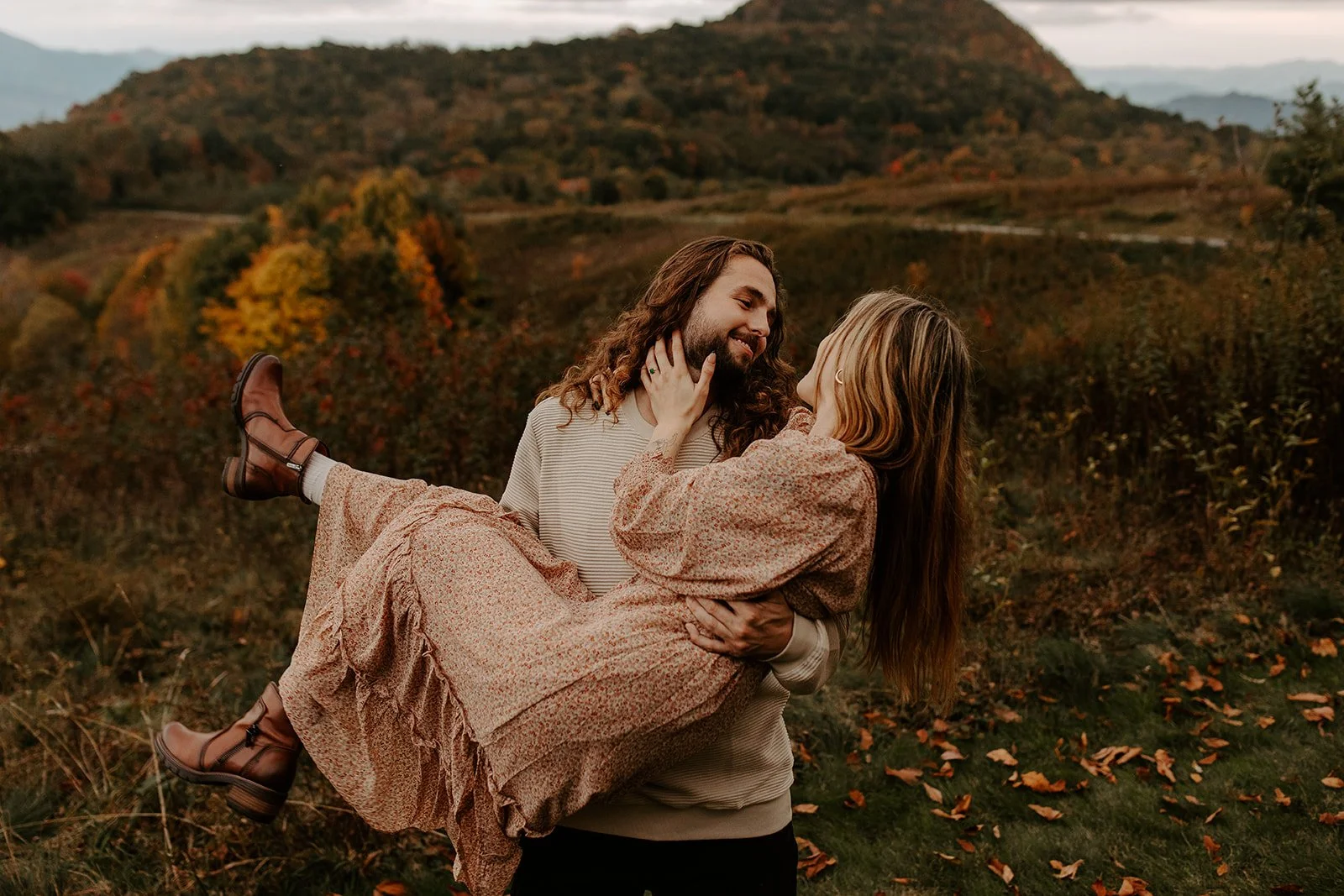 Partner carrying the other in their arms while laughing together in front of vibrant fall foliage and mountain peaks in the Smoky Mountains