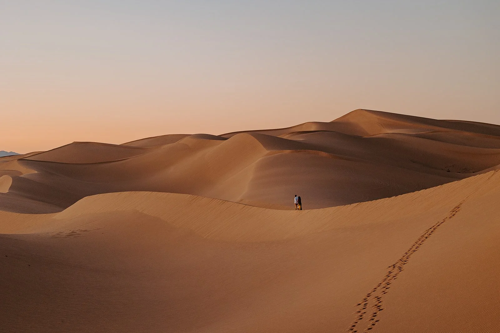 Couple walking across sweeping sand dunes at Hugh T. Osborne Lookout in the Imperial Sand Dunes during sunrise engagement photos