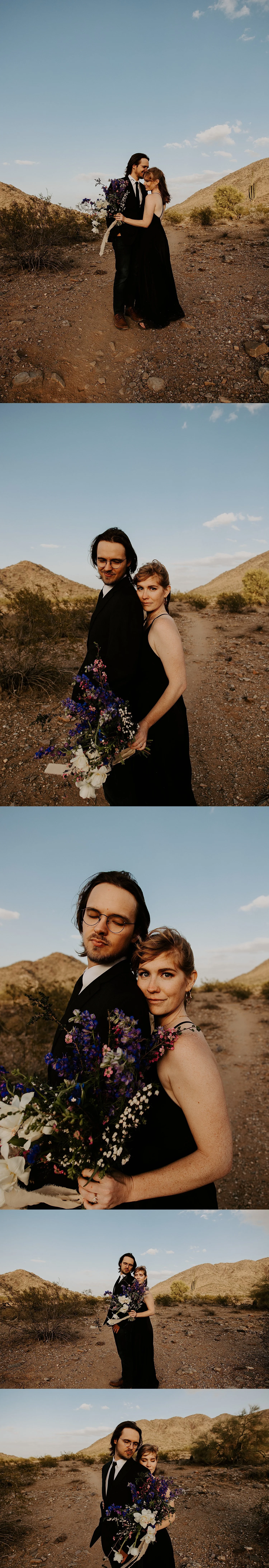 Bride hugging the groom from behind holding a blue, purple, pink, and white bouquet next to their all black wedding attire in the desert.