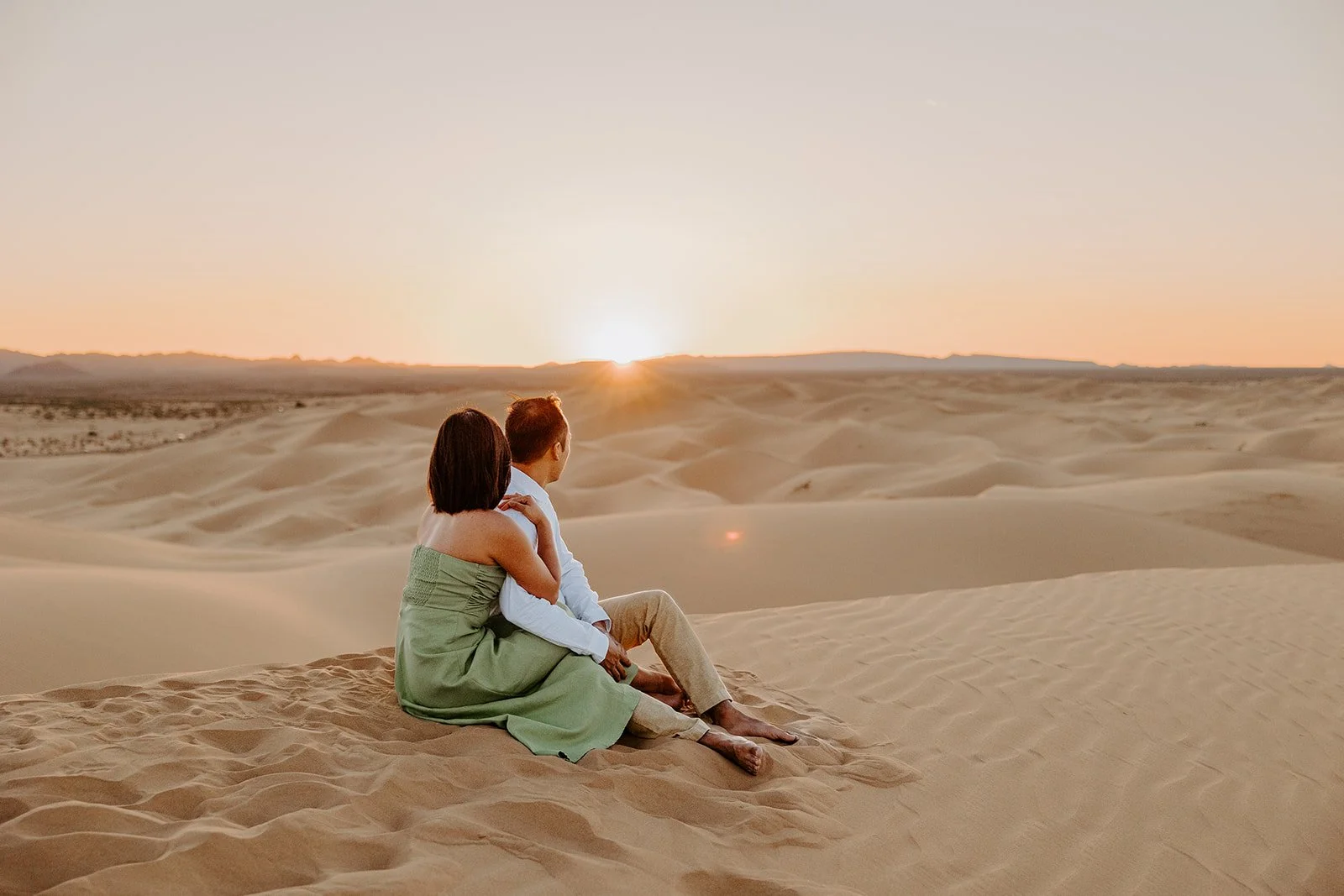 Couple sitting together on a sand dune watching the sunrise over a vast desert landscape