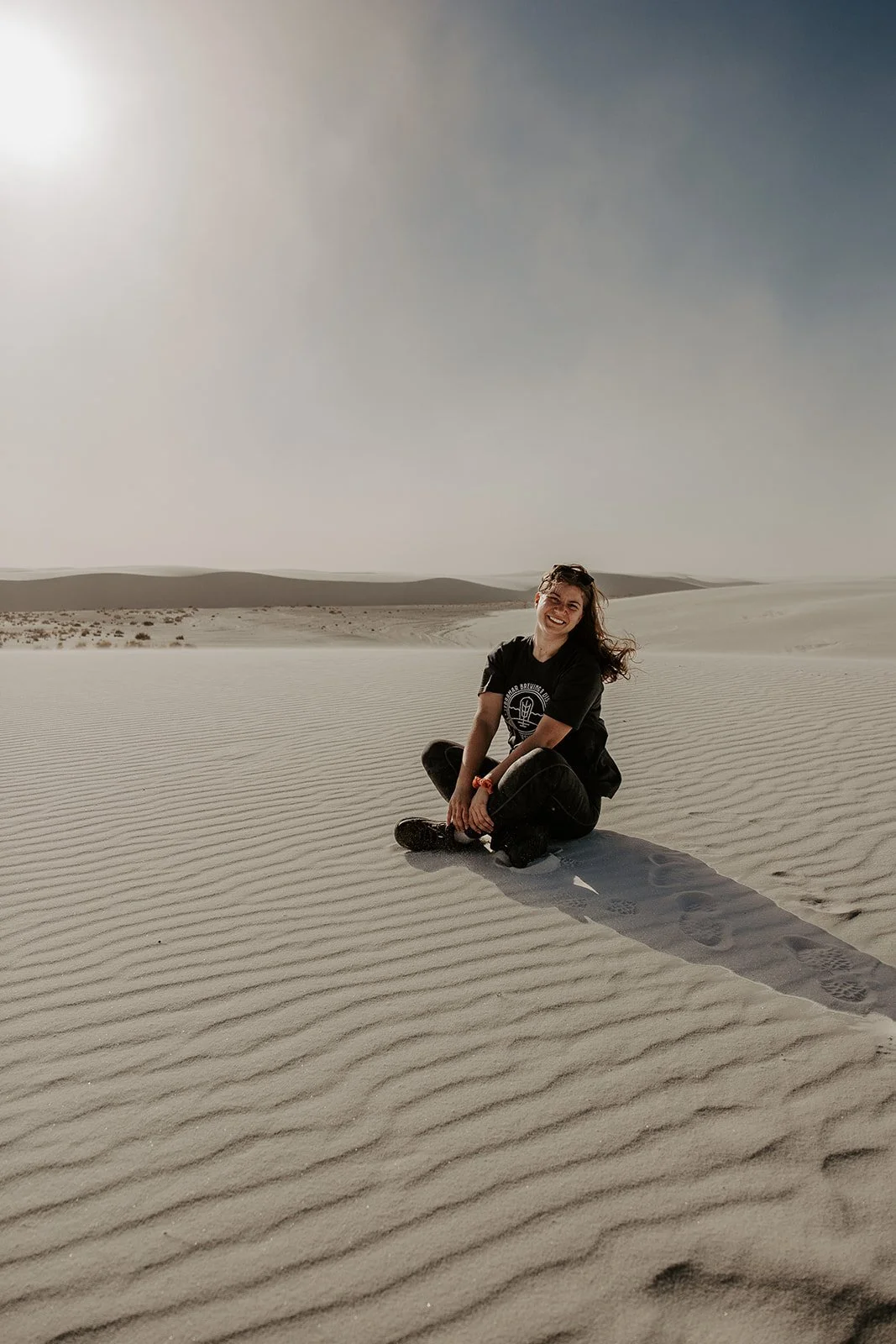 Woman sitting on rippled white gypsum dunes at White Sands National Park in New Mexico under bright desert light