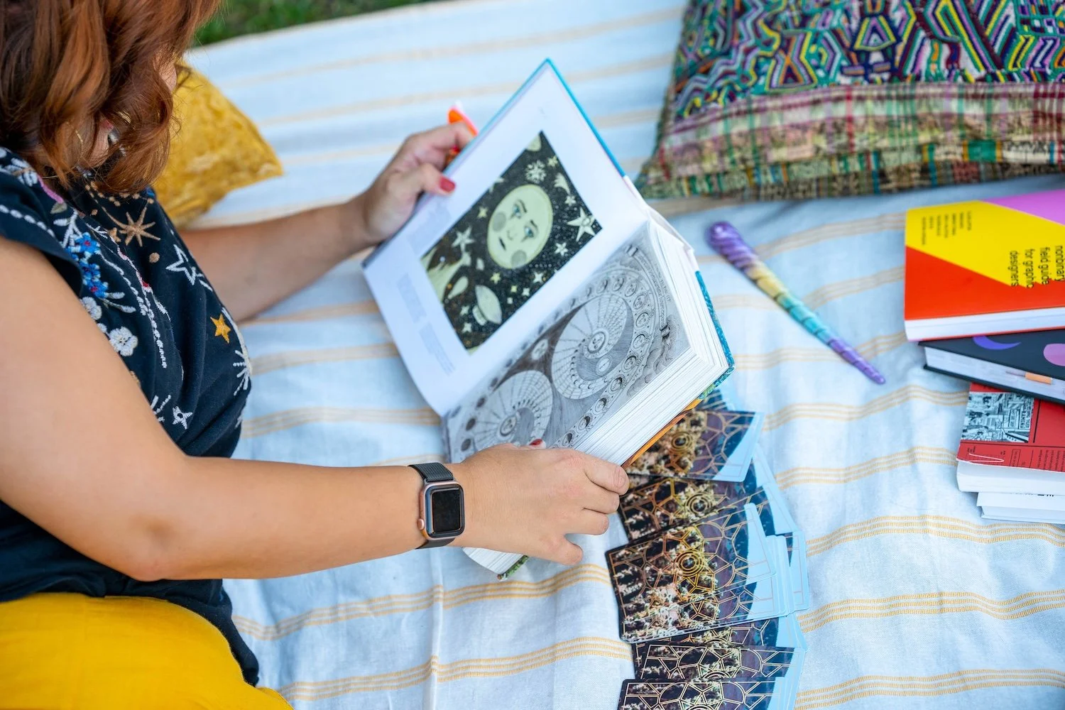 Alex reading a book of celestial illustrations with tarot cards spread on a blanket