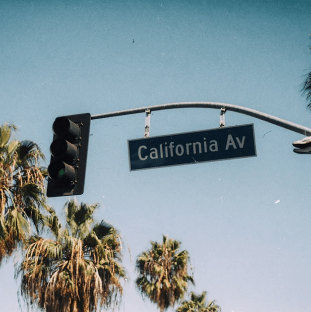 Street sign reading California Ave under traffic lights, with palm trees and a clear blue sky in the background.