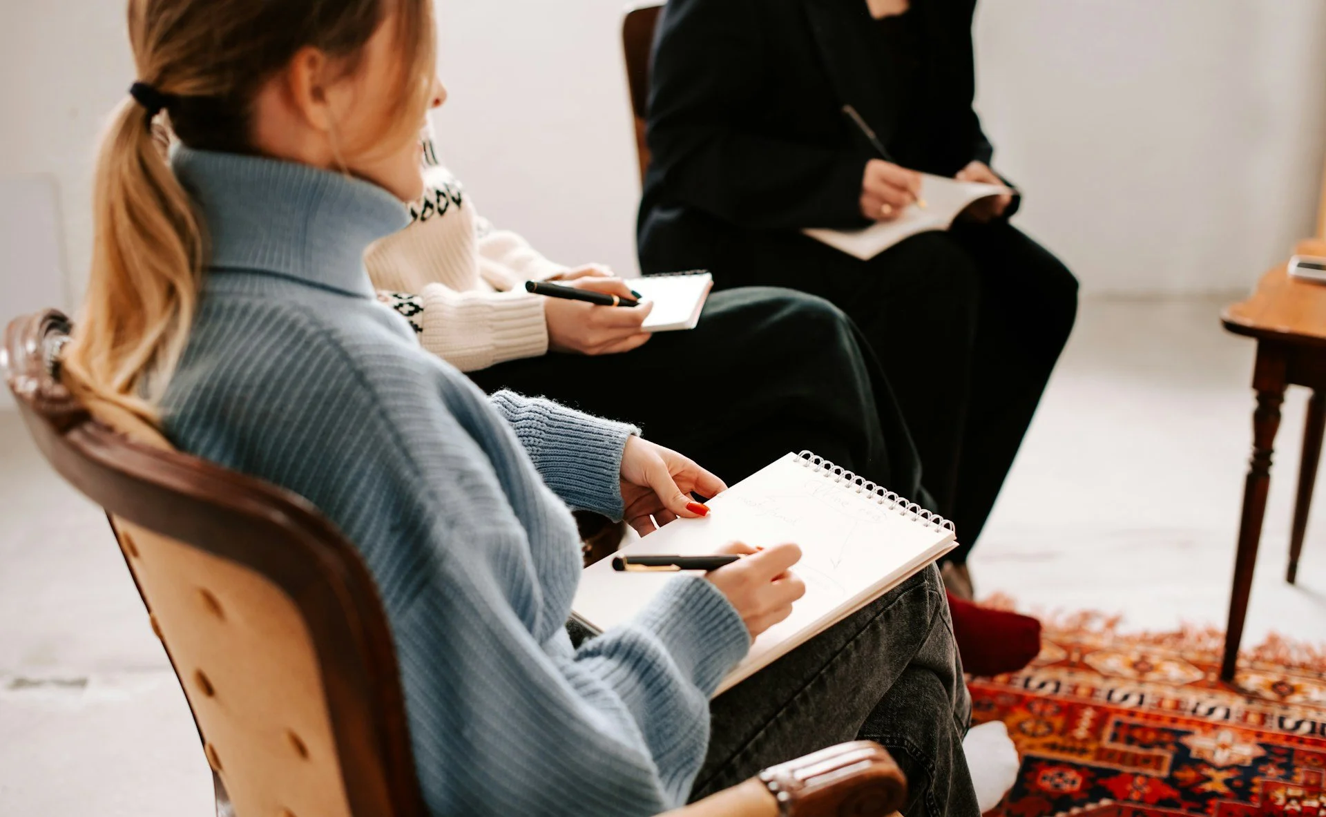 People sitting in a row, taking notes in notebooks during a meeting or workshop.
