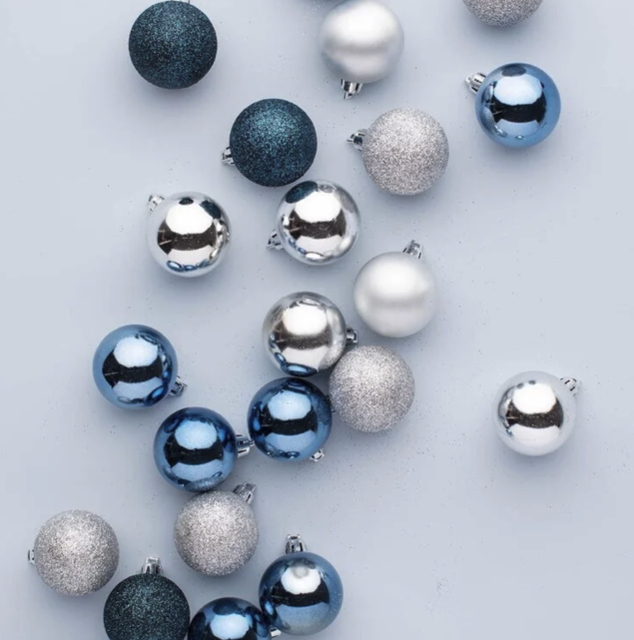 Various Christmas ornaments in blue, silver, and white scattered on a light background.