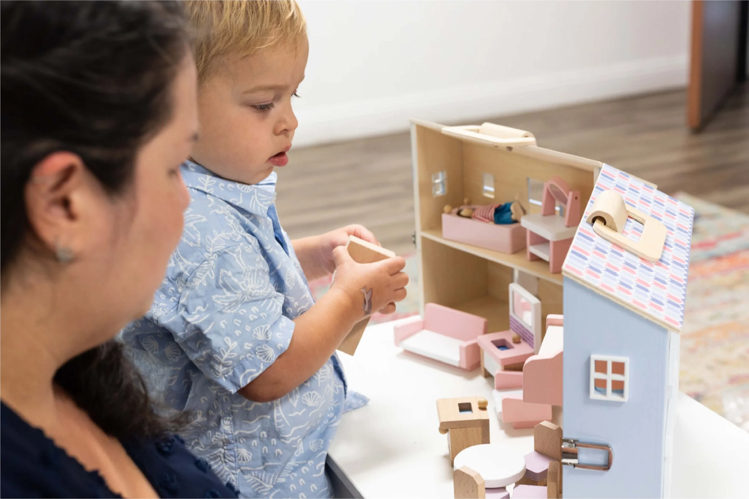 Children playing with a dollhouse at a table.