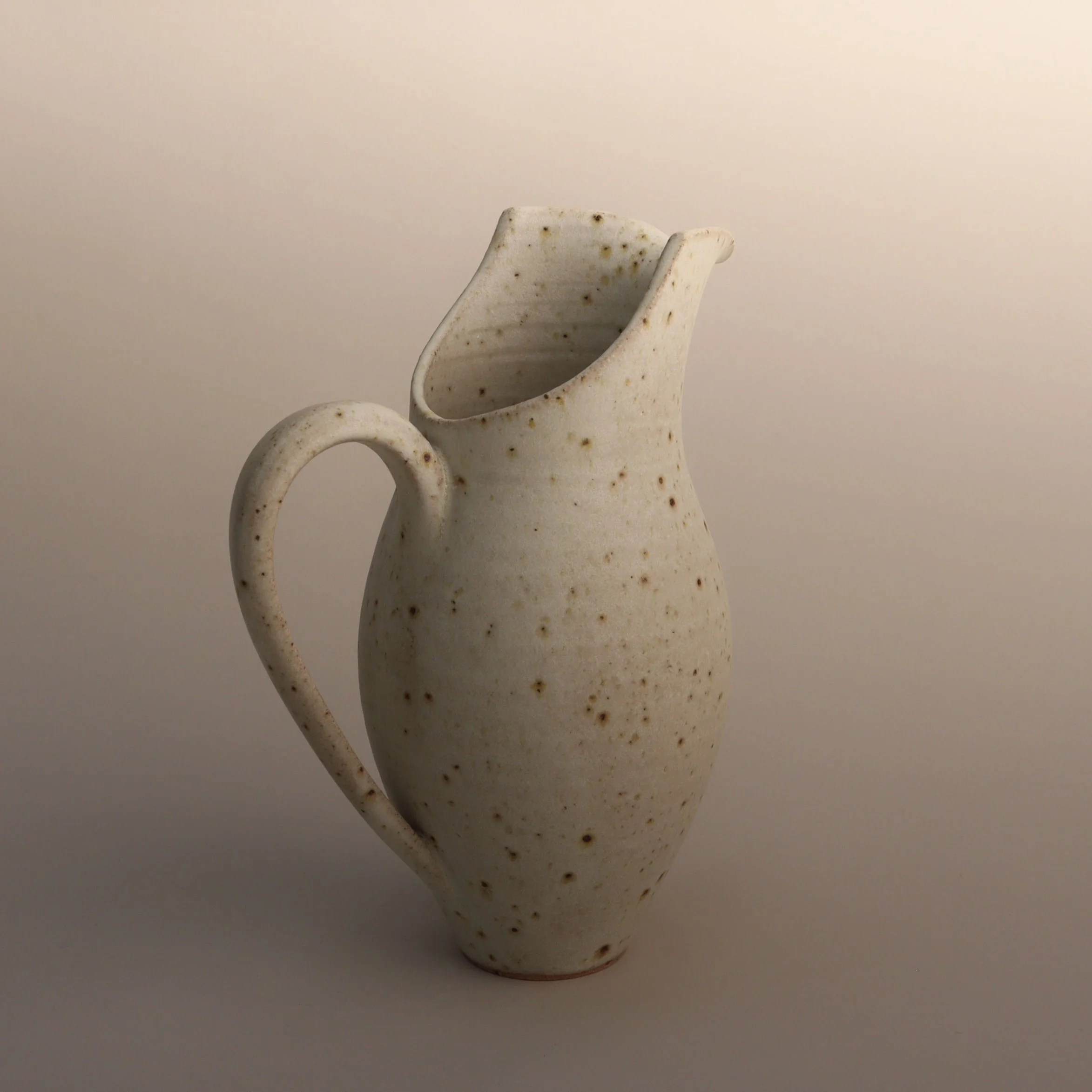 One of Emma Baldwin's flecked white ceramic jugs with a curved handle, set against a plain background.