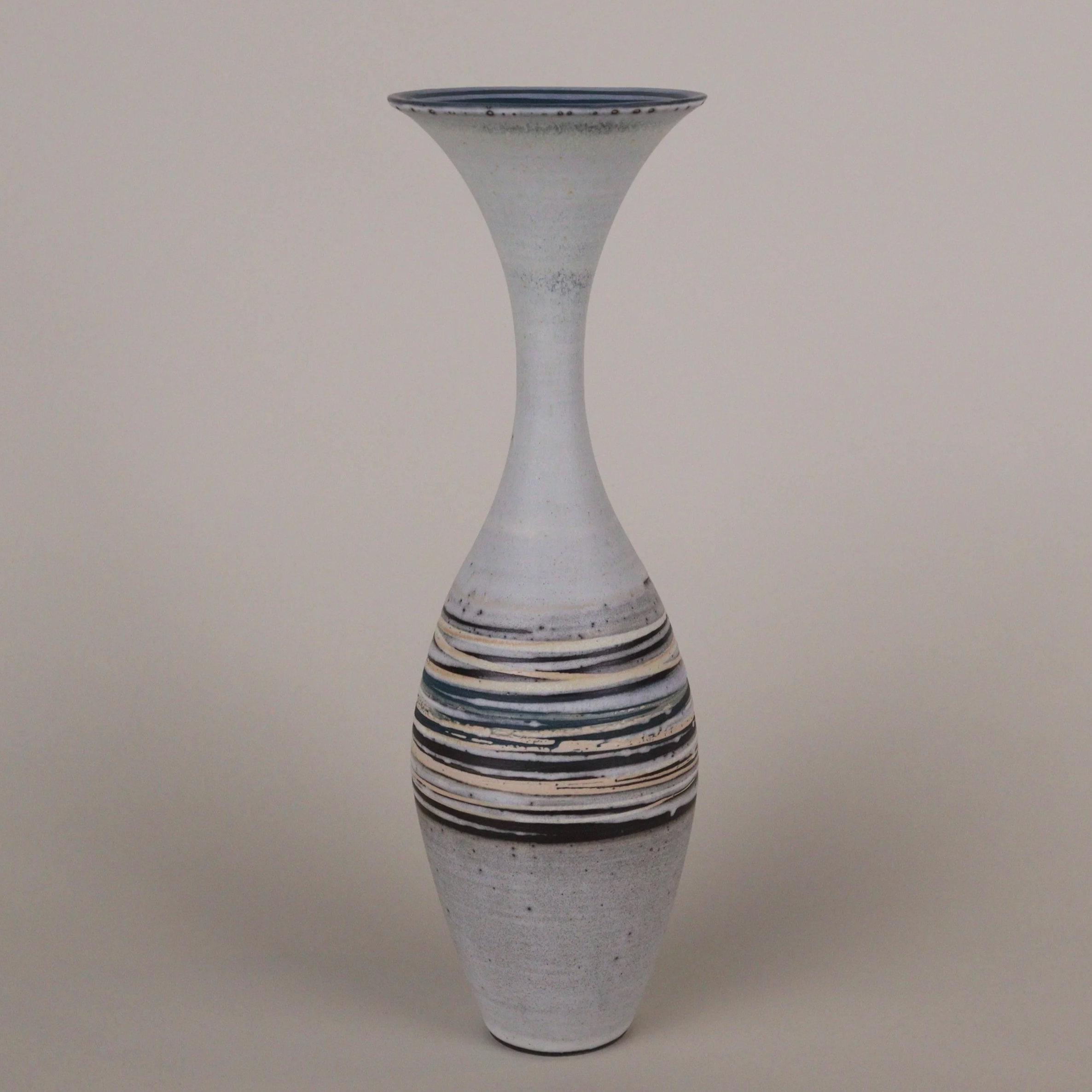 A tall ceramic vase with a narrow neck, featuring horizontal black, blue, and beige stripes near the middle, against a plain light background.