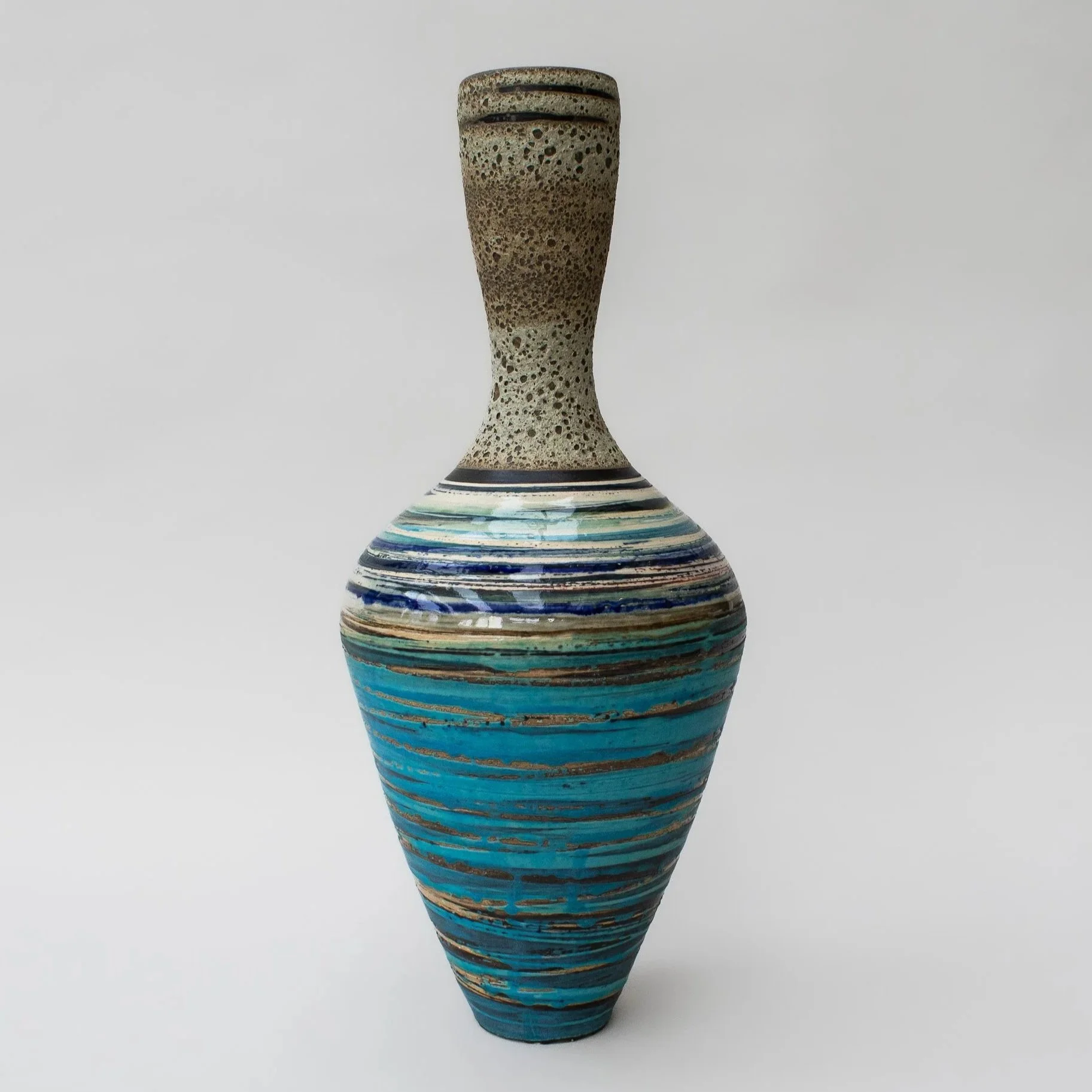 Colorful ceramic vase handmade by Emma Baldwin with horizontal stripes in blue, turquoise, brown, and white, featuring a textured top section, set against a plain white background.