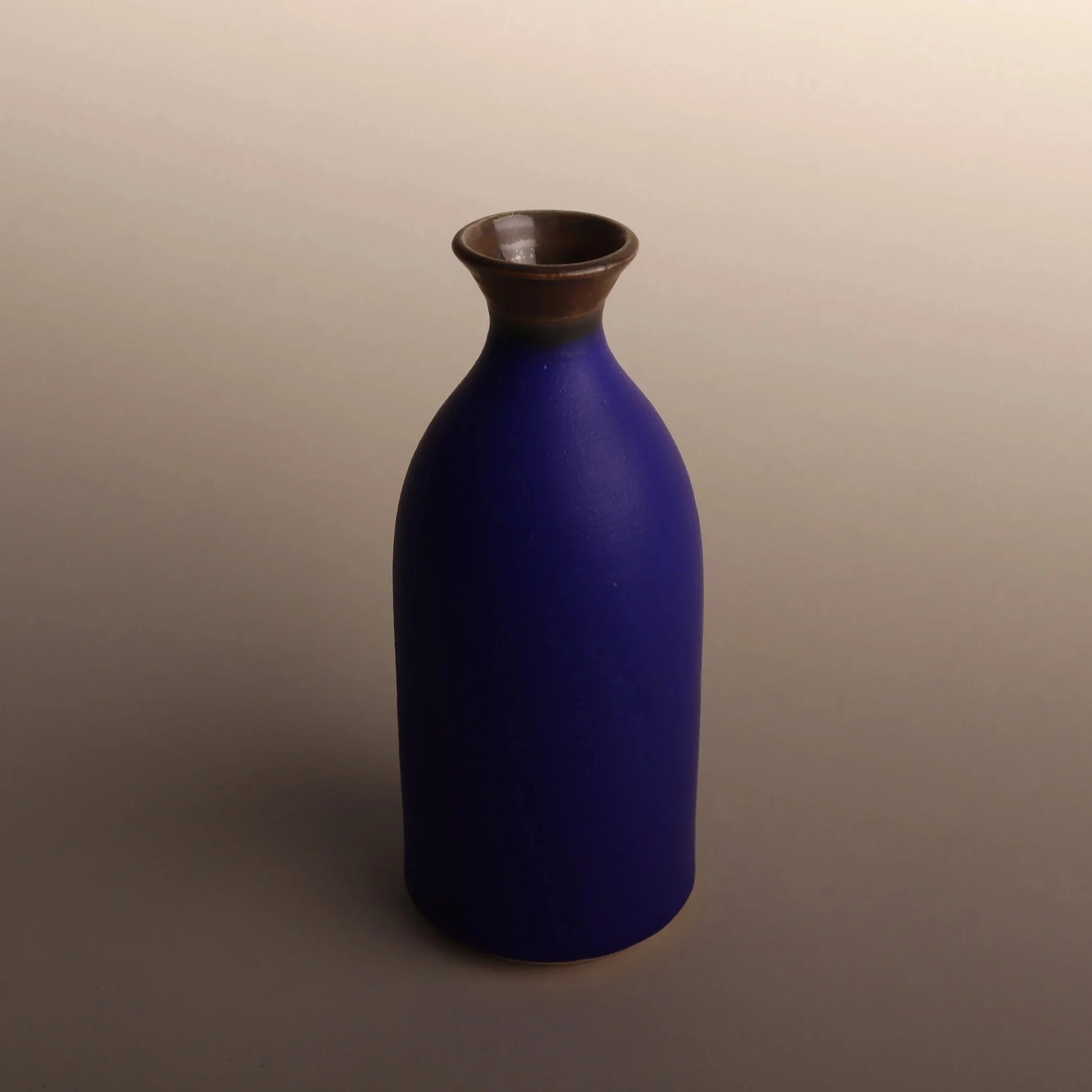 One of Emma Baldwin's ceramic bud vases with an intense matt blue body and a bronze neck, set against a neutral background.