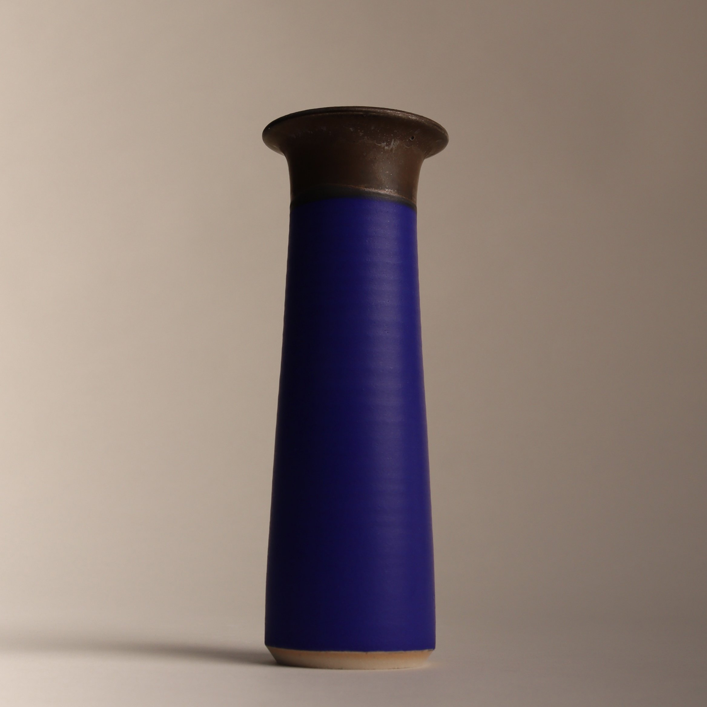 One of Emma Baldwin's ceramic stem vases with a wide bronze top and an intense matt blue body set against a neutral background.