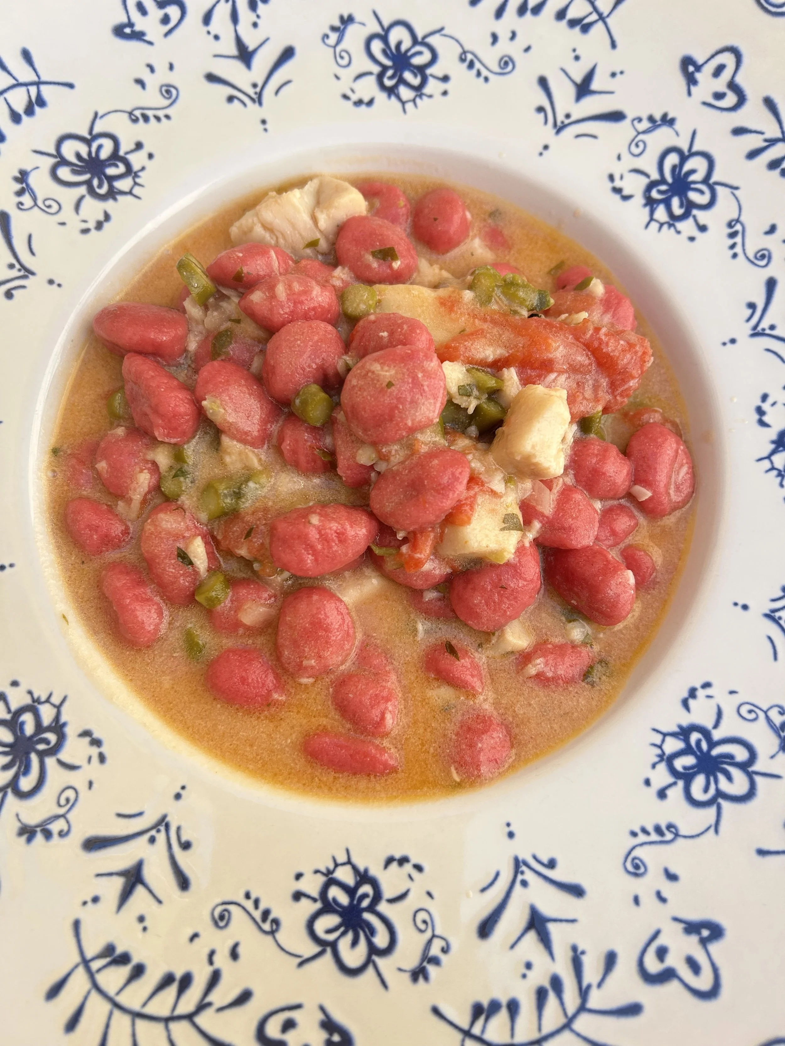 A bowl of gnocchi with beetroot  and some green peas in a creamy sauce, served in a white bowl with a blue floral pattern.