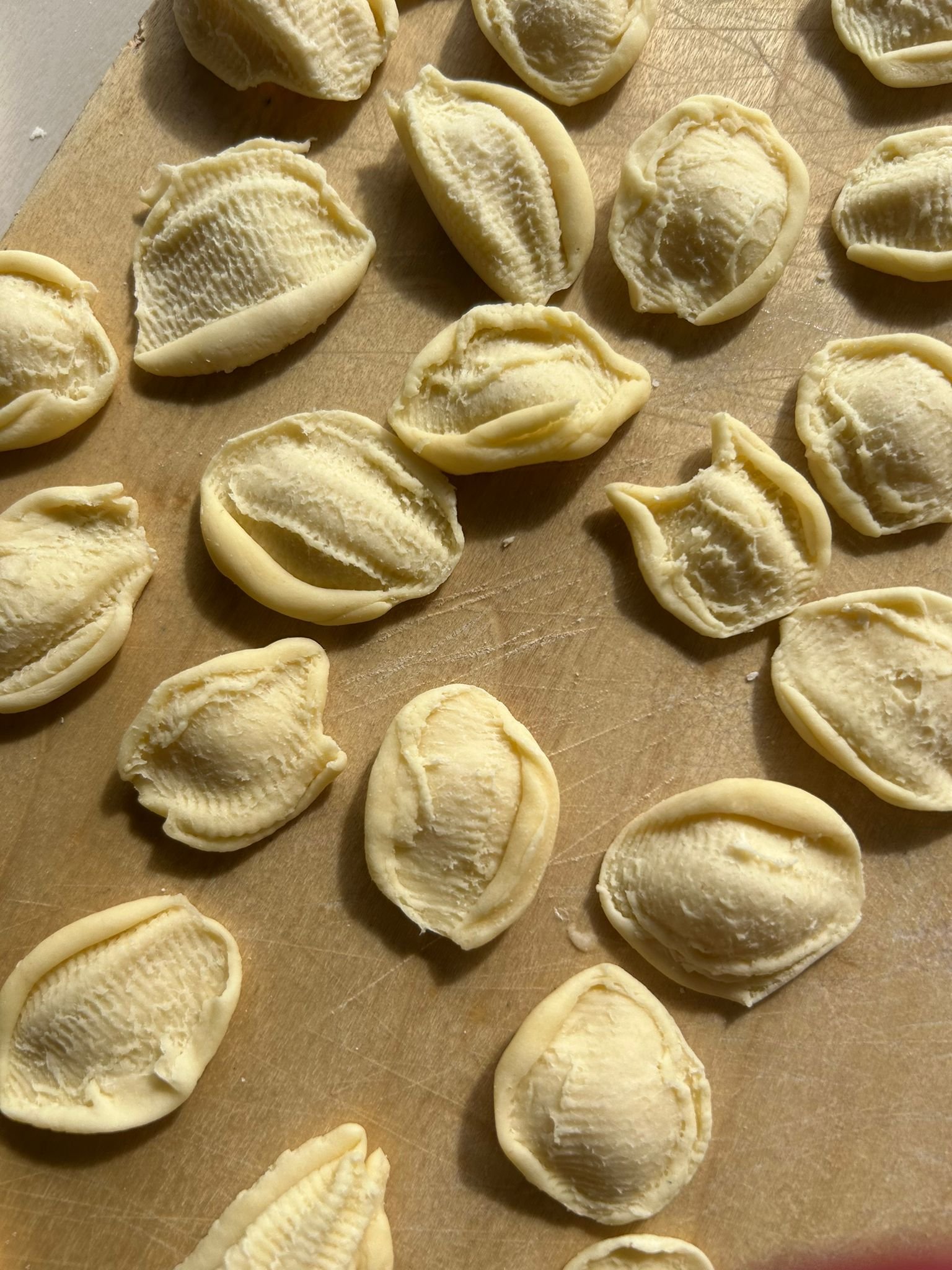 Uncooked handmade orrechietti on a wooden surface, ready to be cooked.