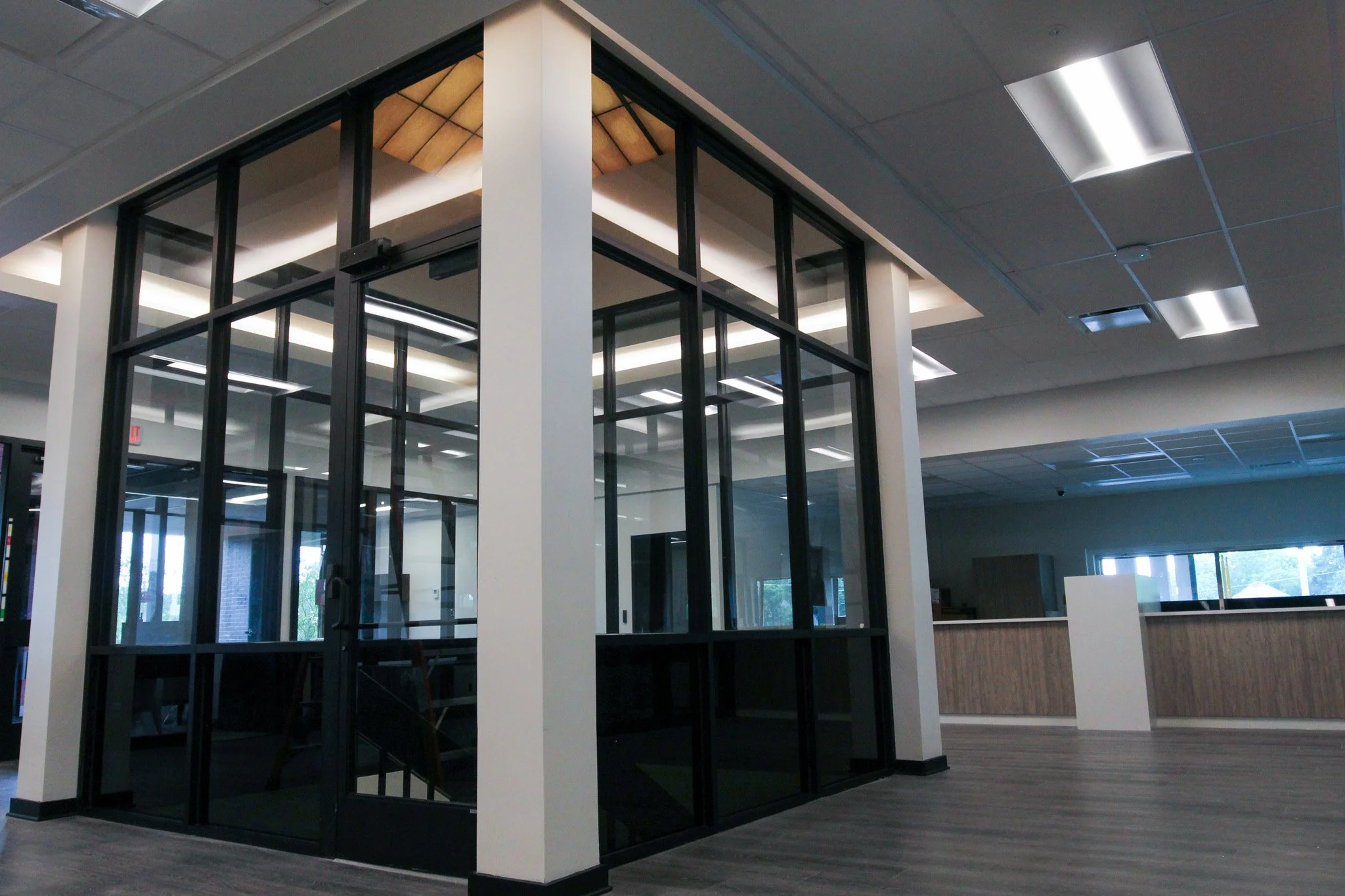 An interior view of the modern offices at Simmons Bank in Athens, TN with a glass enclosure, framed in black metal, beneath a ceiling with fluorescent lighting fixtures.