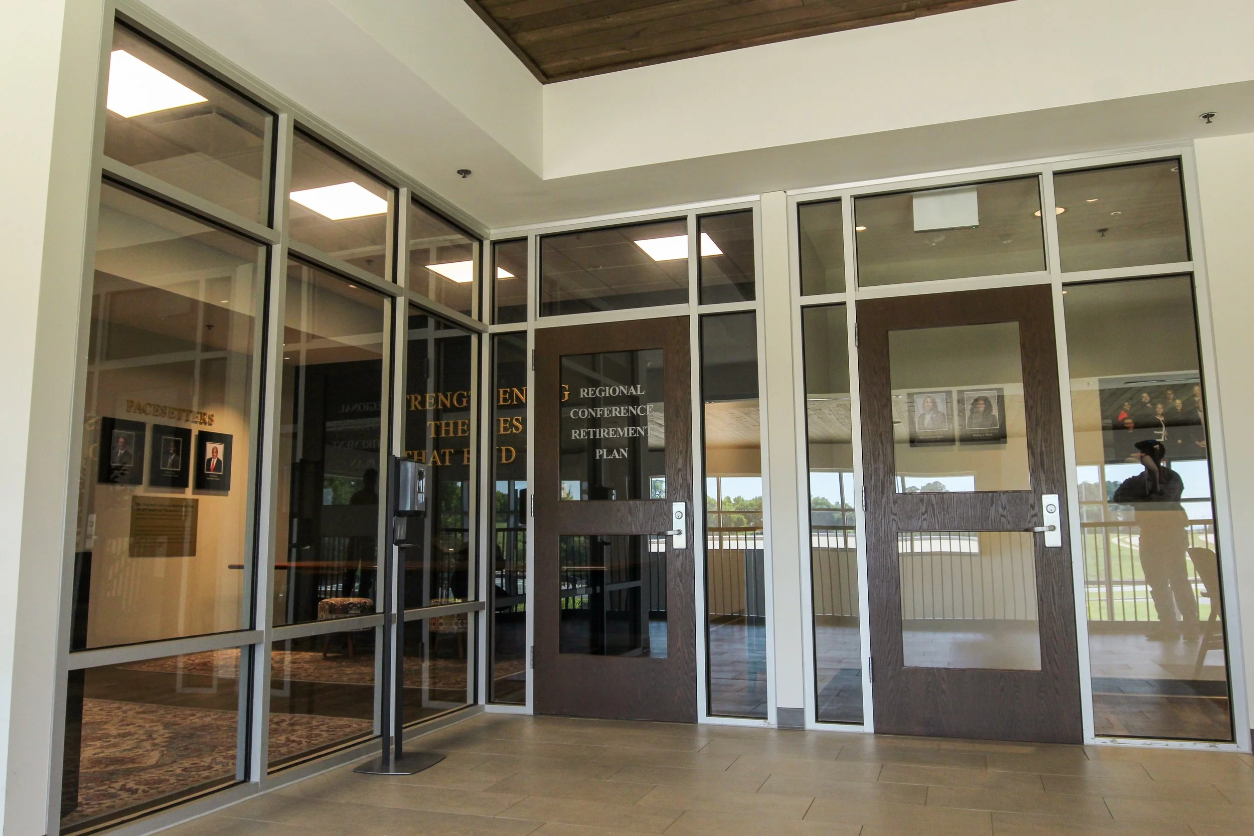 Interior view of a building entrance with glass doors and panels, with a hallway visible through the doors and windows, including framed photographs on the wall. Design - build by P&C Construction, Inc. - Chattanooga, Tn.