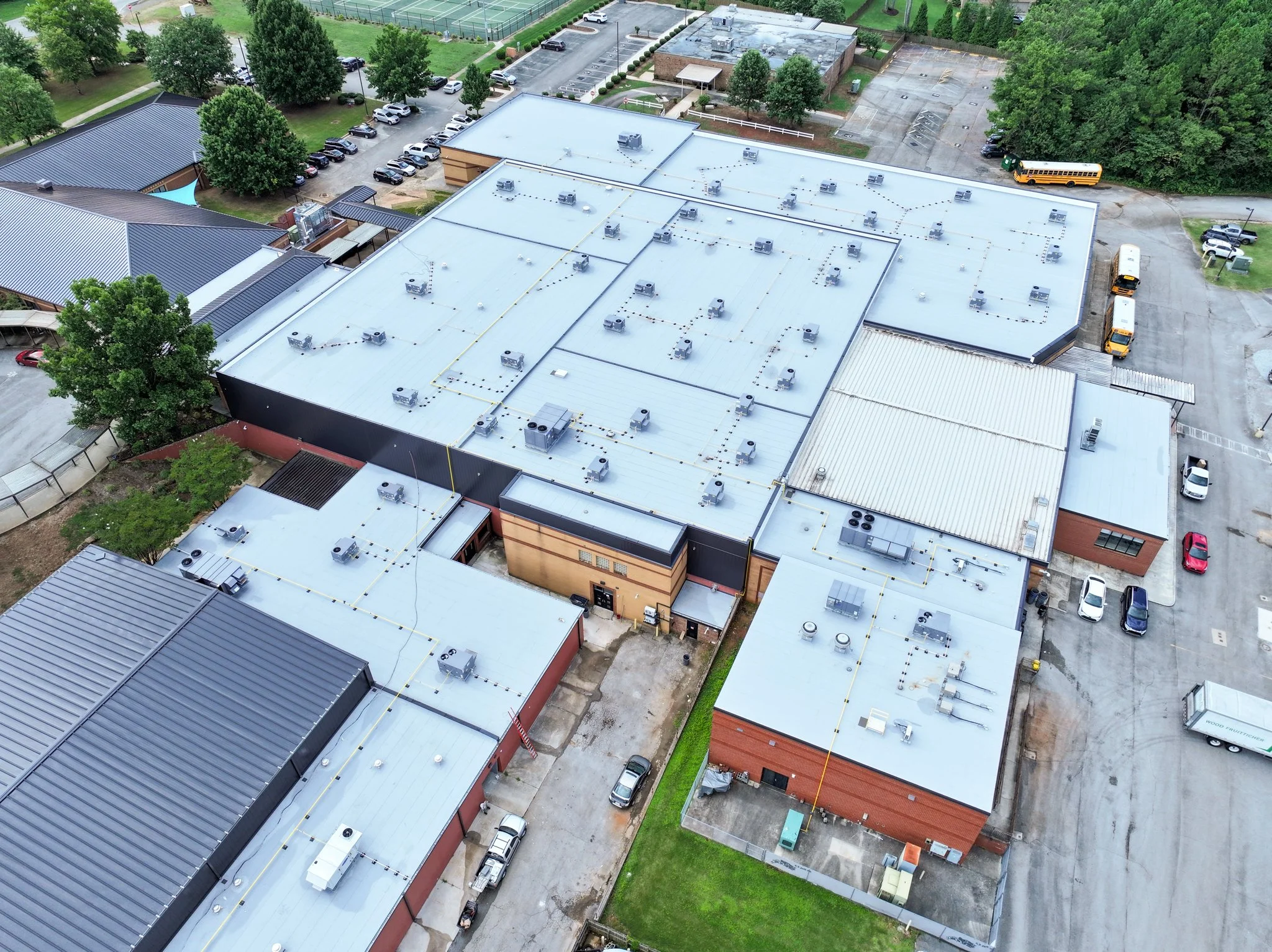 An aerial view of Discovery Middle School building with a metal roof, surrounded by parking lots with numerous cars and green trees.