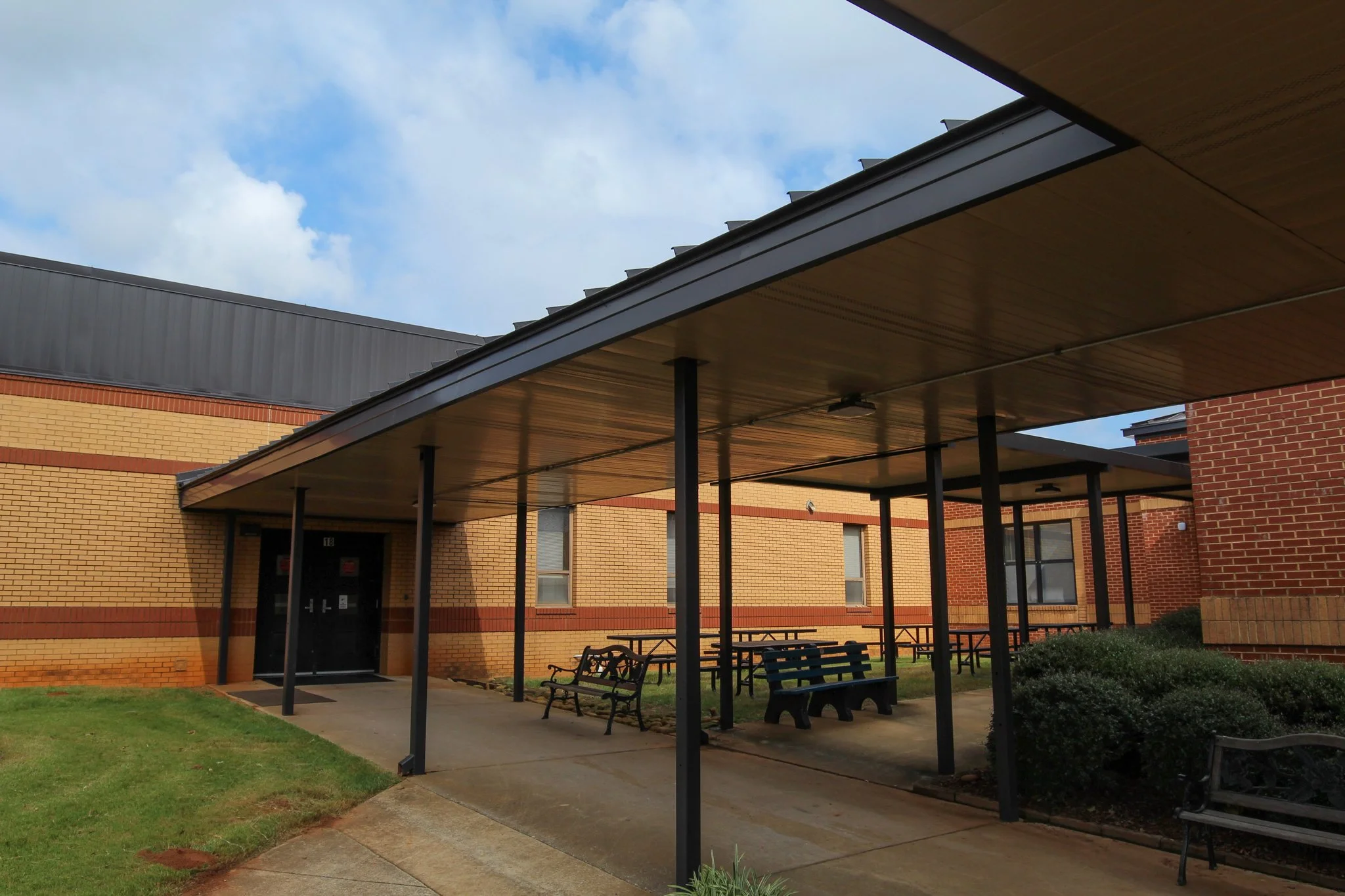 A brick building with a covered walkway and benches outside, under a partly cloudy sky.