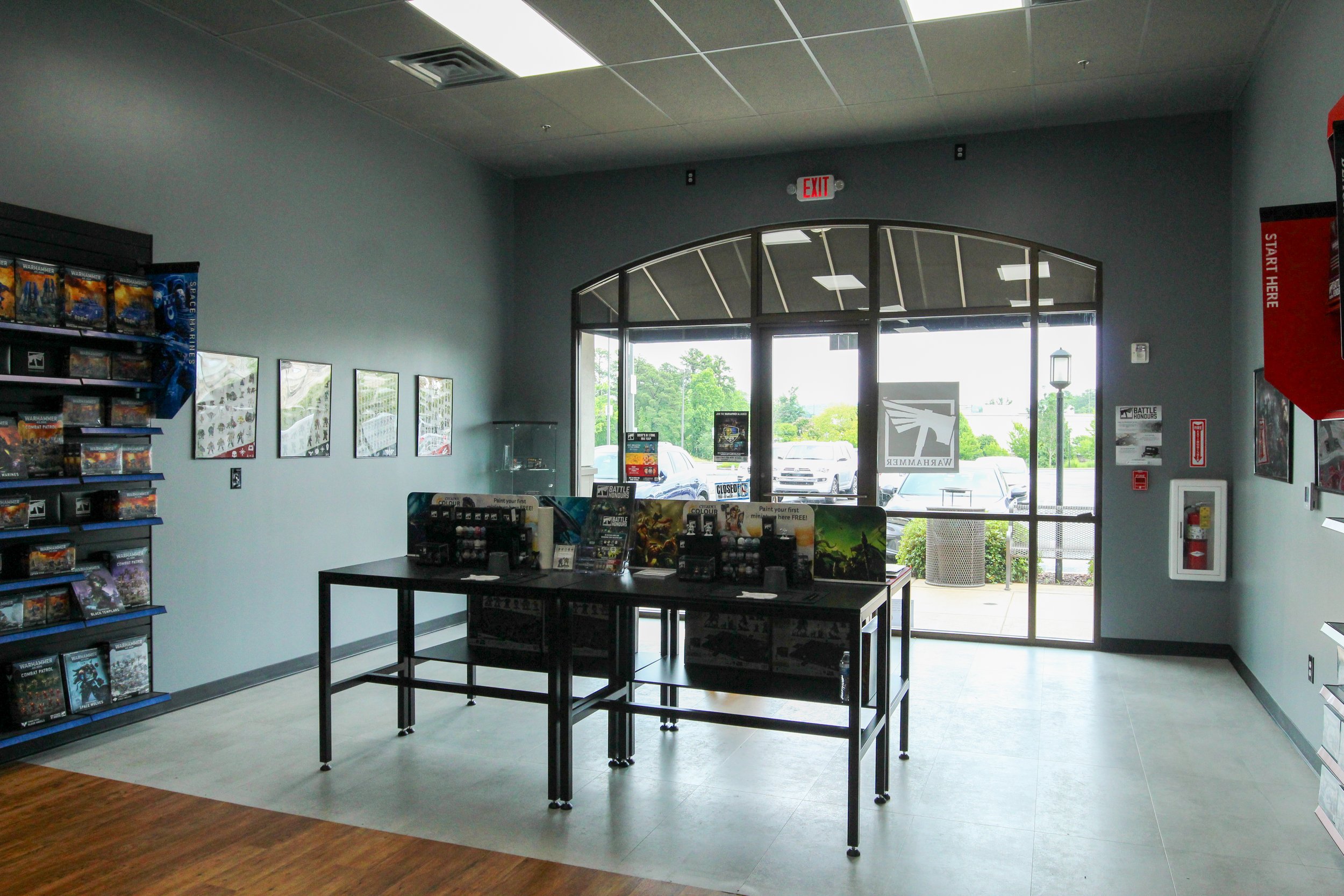 Inside a toy and game store, with shelves of boxed games on the left, display tables in the center, and glass doors leading outside at the back, letting in natural light. Remodeled by P&C Construction, Inc. - Chattanooga, Tn.