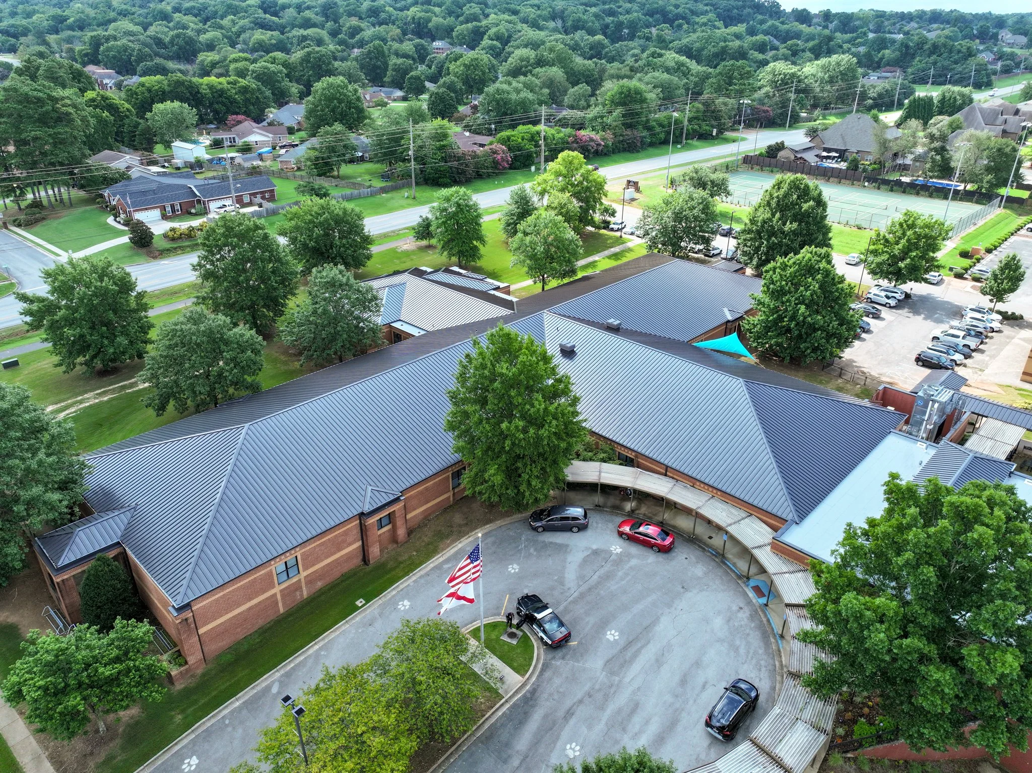 An aerial view of Discovery Middle School, trees, a tennis court, parking lot, and a school building with a curved driveway and flagpole.