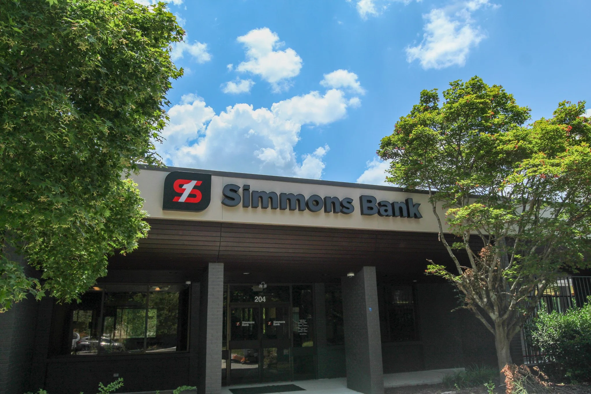 Exterior of Simmons Bank building in Athens, TN with trees and a blue sky with clouds.