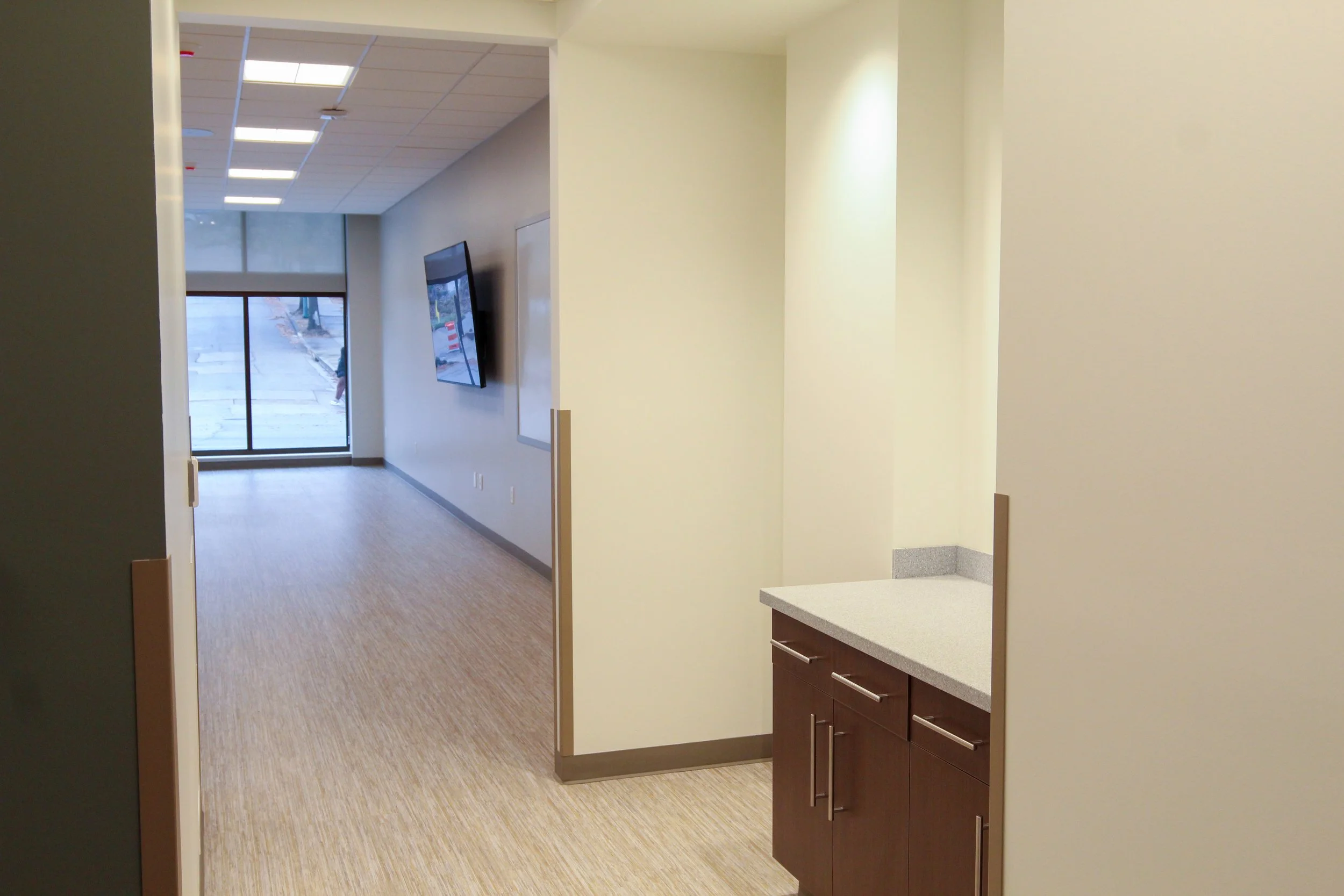 Empty corridor in a modern office building with a mounted TV and glass door at the end.