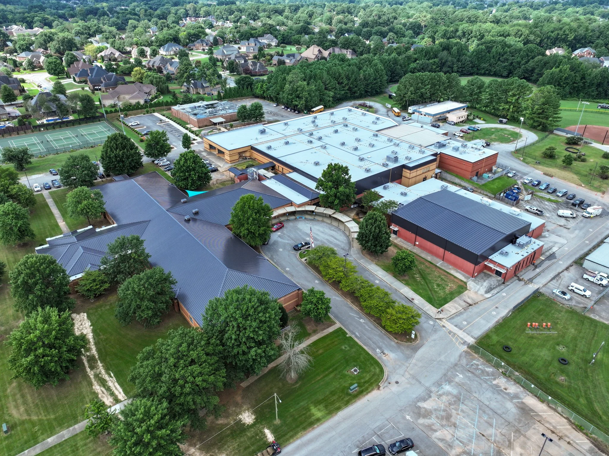 Aerial view of Discovery Middle School, trees, and a large building with a flat roof surrounded by parking lots and sports courts.