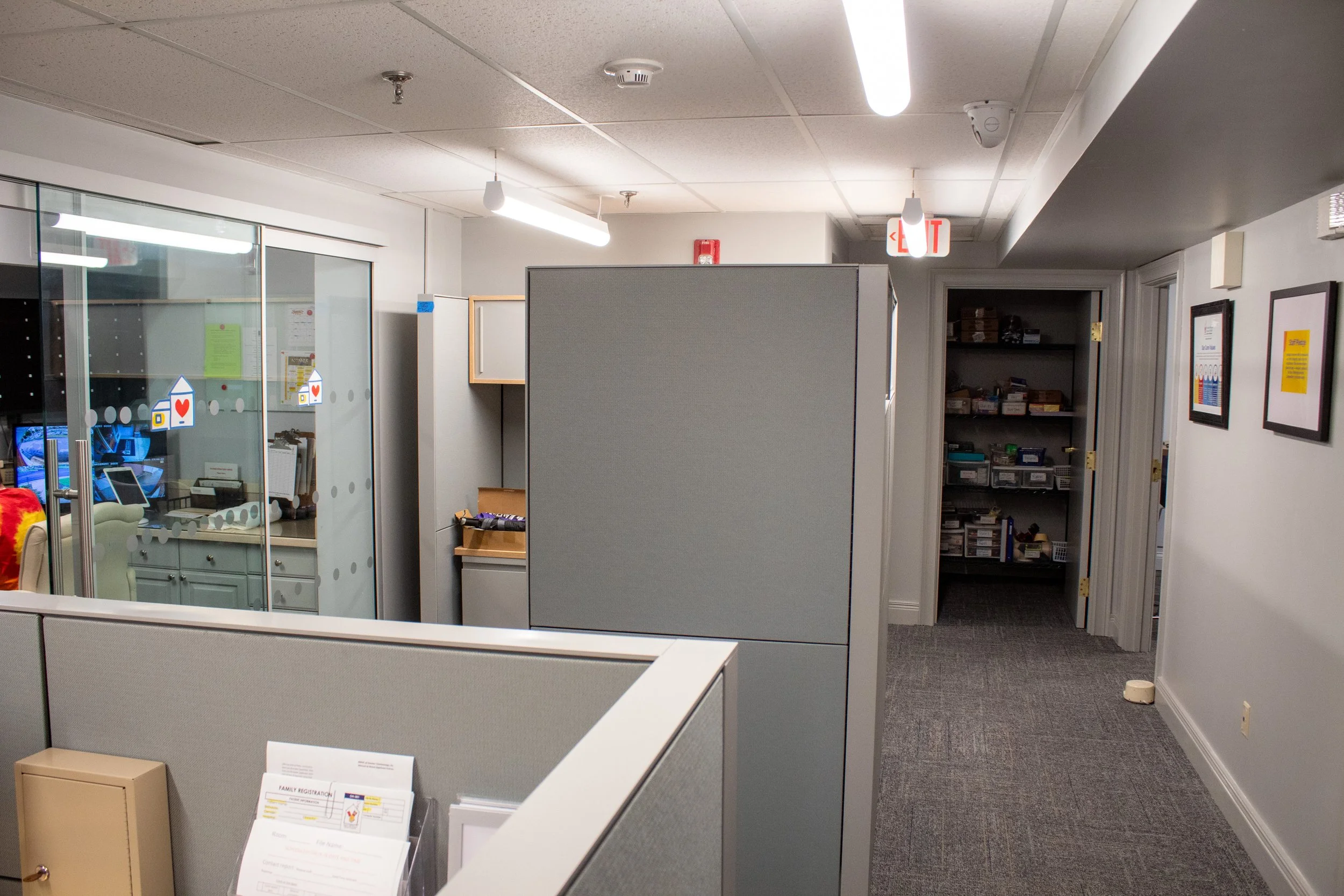 Office cubicles and hallway with shelves and framed posters on the wall.