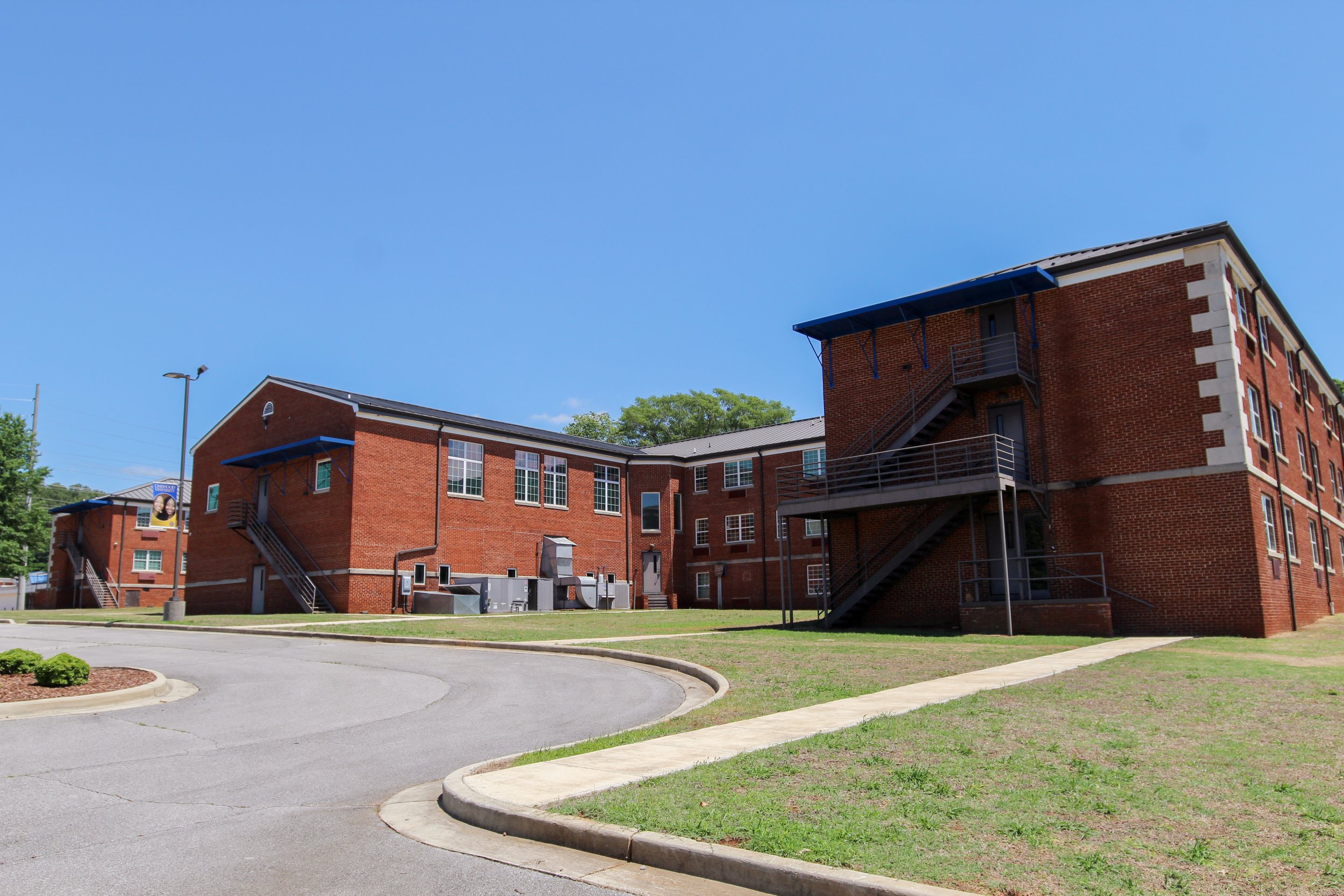 A red brick apartment complex with external metal staircases and a fire escape, set under a clear blue sky with some trees in the background. Historic Remodeled by P&C Construction, Inc. - Chattanooga, Tn.