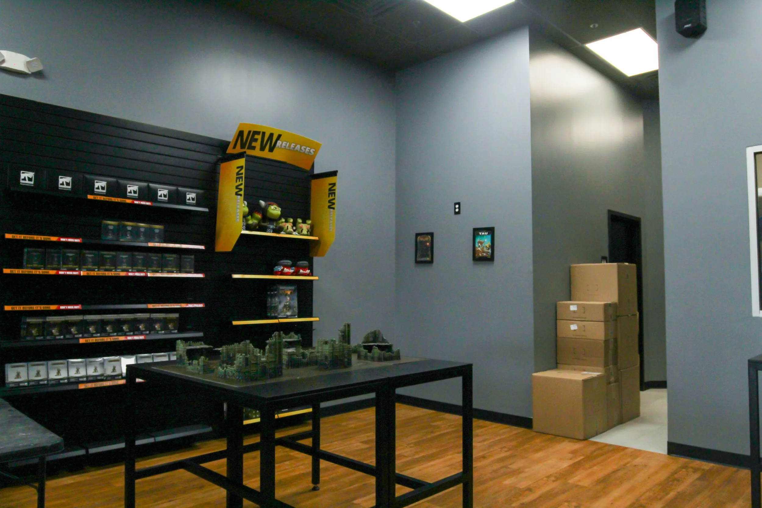 A room with gray walls and ceiling with fluorescent lighting, featuring shelves displaying toys and games, boxes stacked in the corner, and a table with a miniature city model. Remodeled by P&C Construction, Inc. - Chattanooga, Tn.