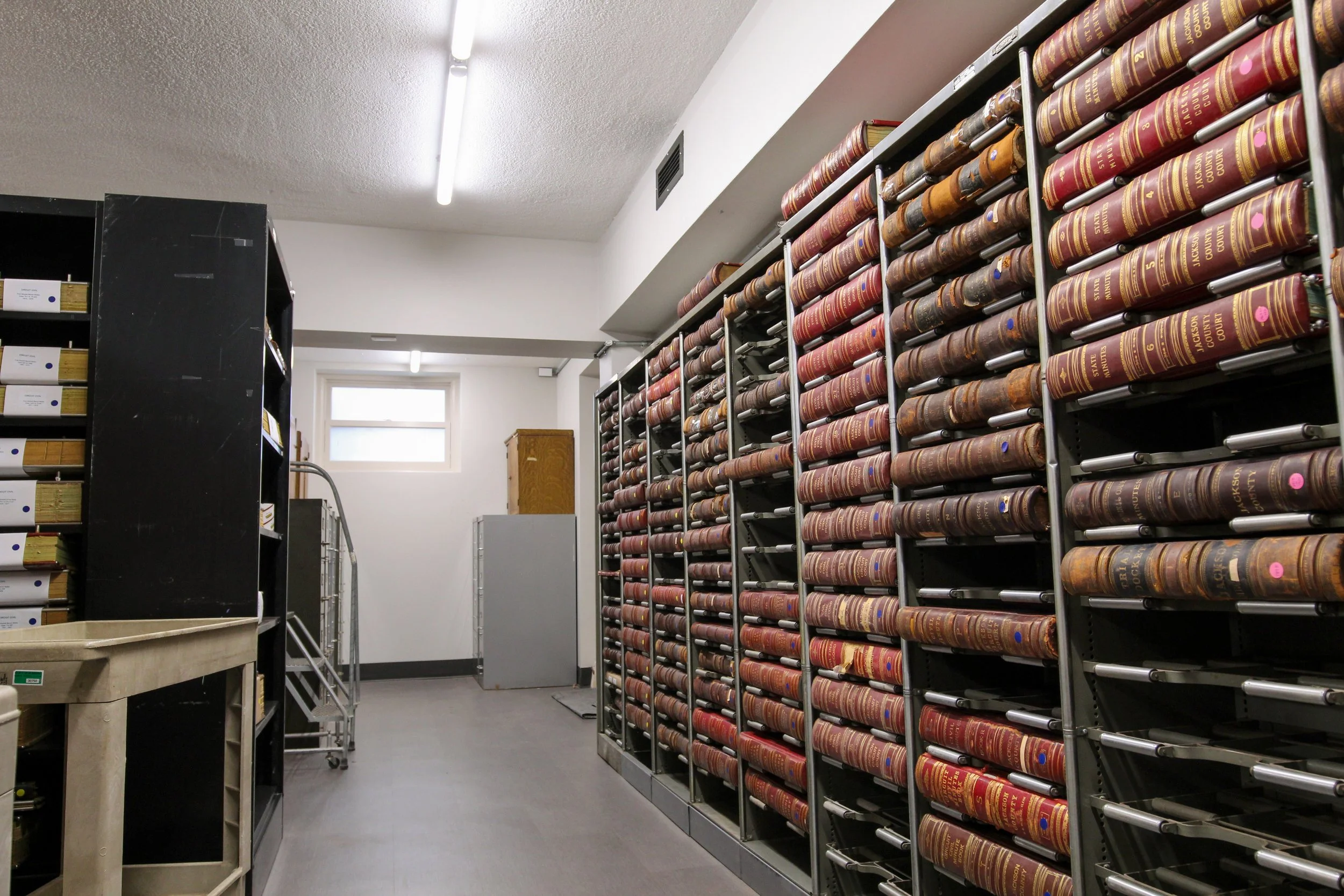A storage room with metal shelves filled with legal books, a small window, and a black cabinet with files.