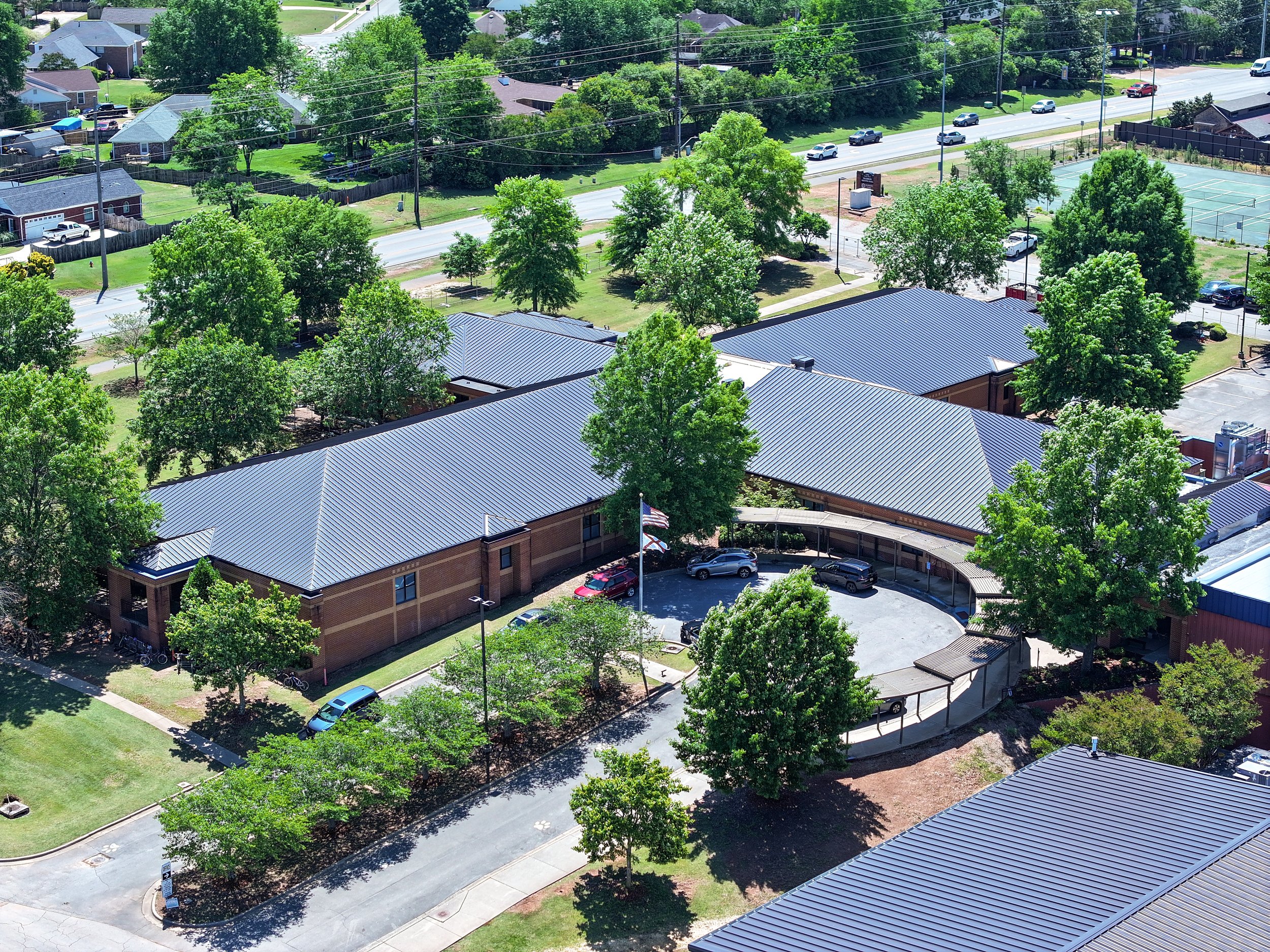 An aerial view of a residential area with trees, houses with metal roofs, a road with cars, and a tennis court surrounded by a fence. Remodeled by P&C Construction, Inc. - Chattanooga, Tn.