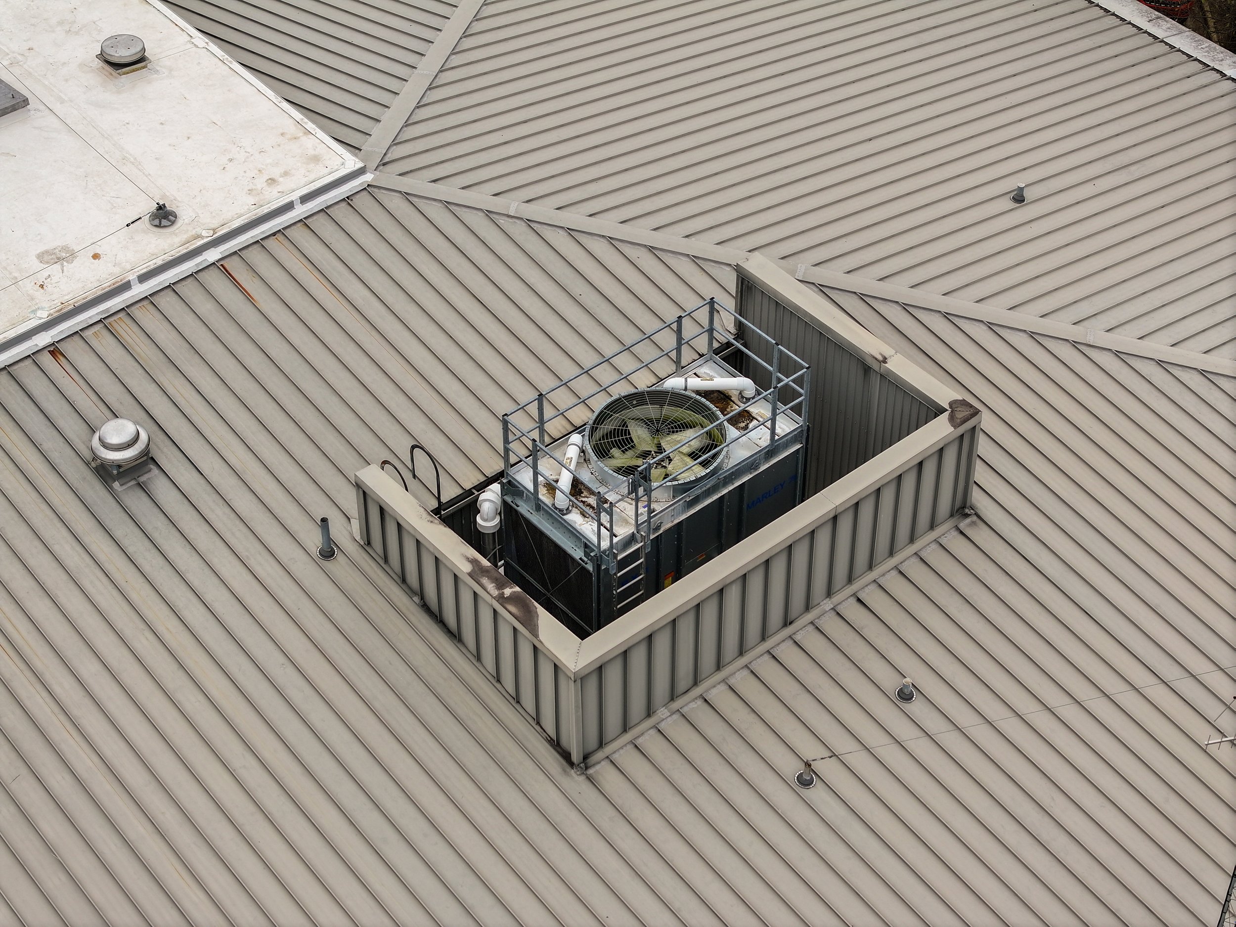 A rooftop with beige metal panels and an HVAC unit in a metal enclosure.