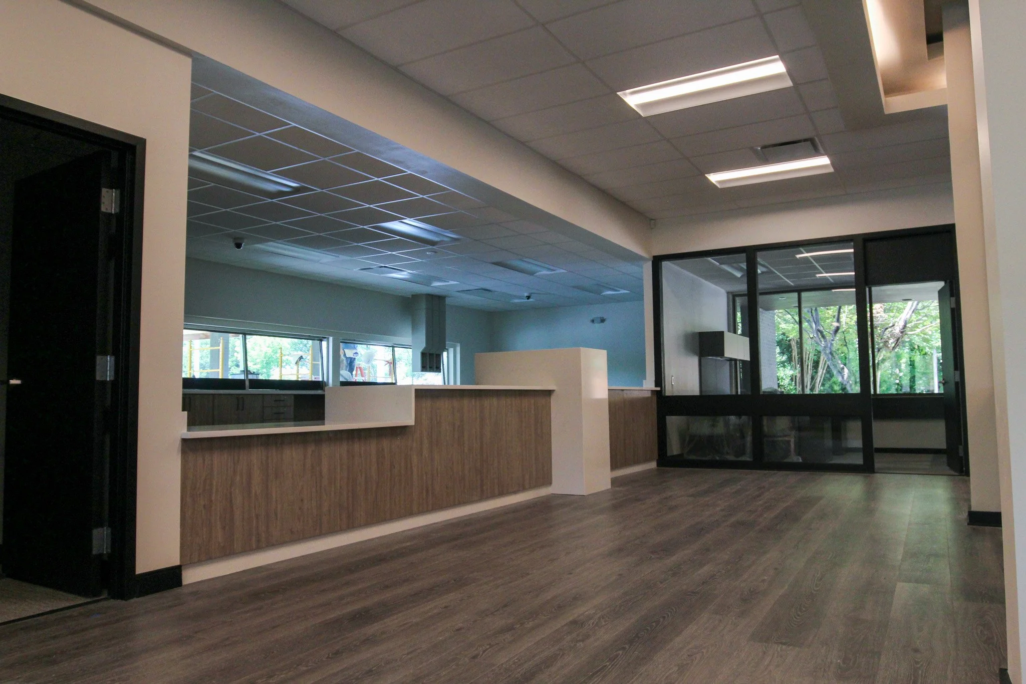 Interior view of the reception area of Simmons Bank in Athens, TN with wood flooring, a reception desk with wood paneling, large windows, and ceiling lights.