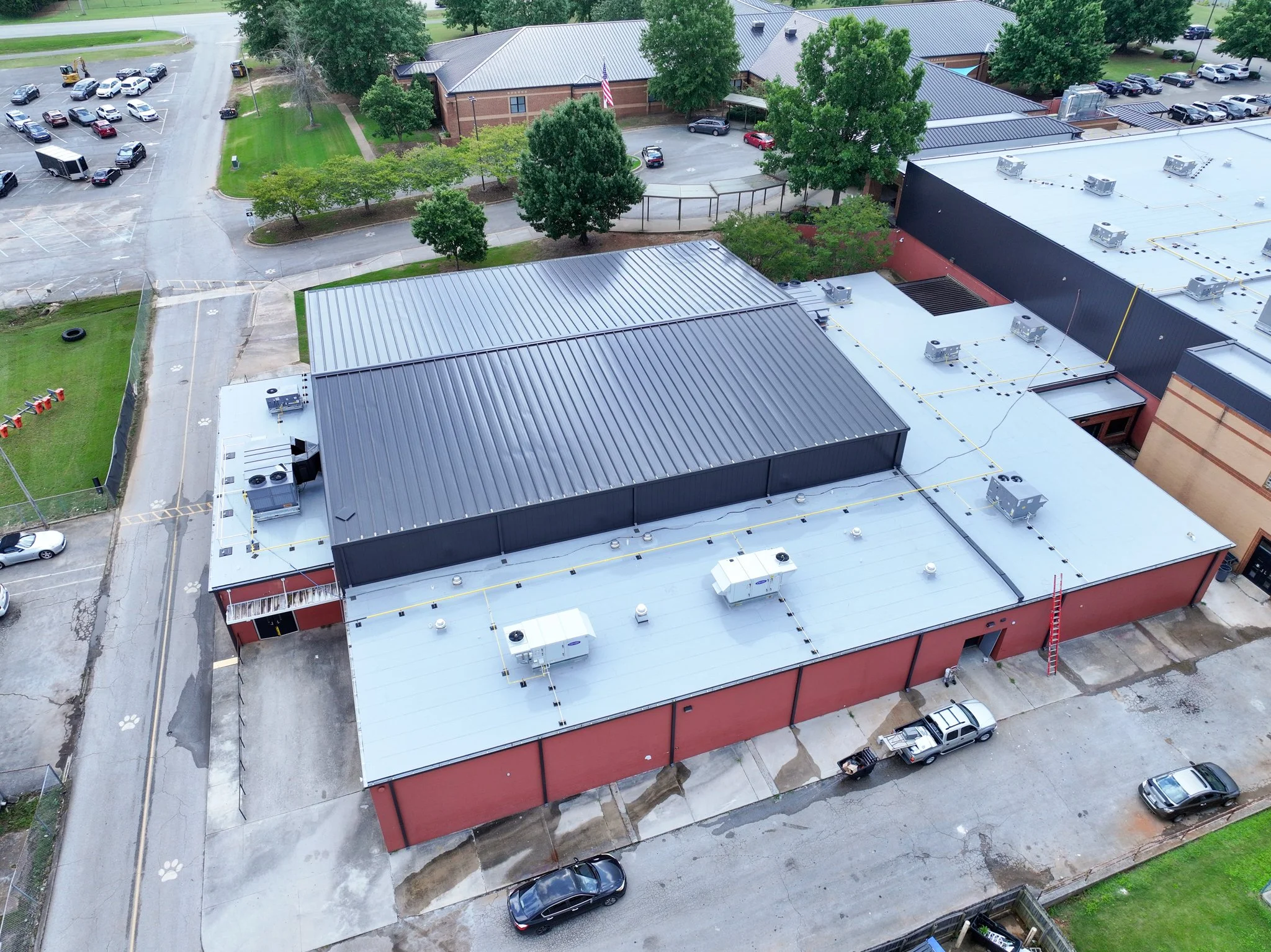 Aerial view of Discovery Middle School with a flat roof equipped with HVAC units, surrounded by parking lots, trees, and adjacent structures.