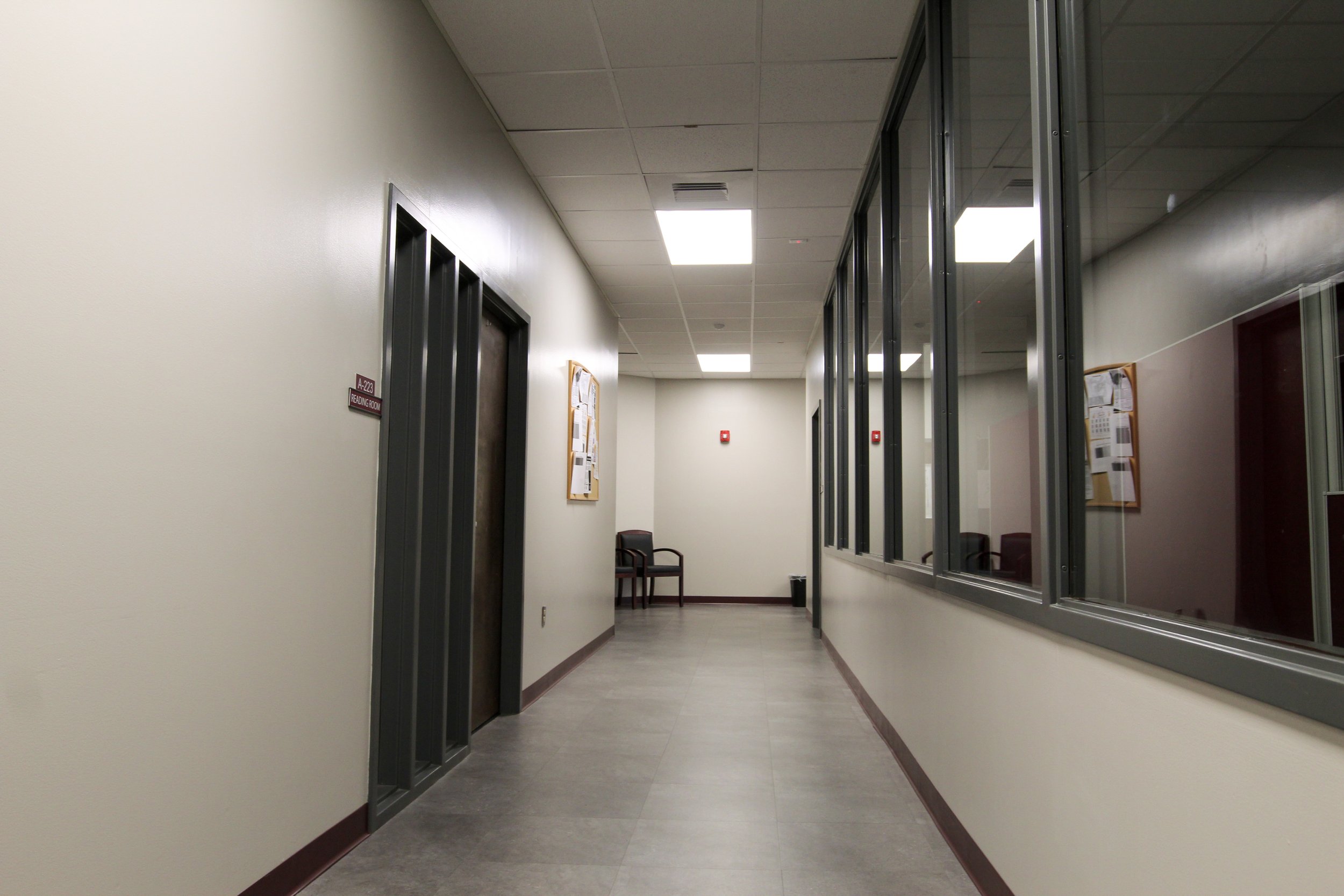 Empty hospital hallway with an elevator to the left and waiting chairs at the end of the corridor.